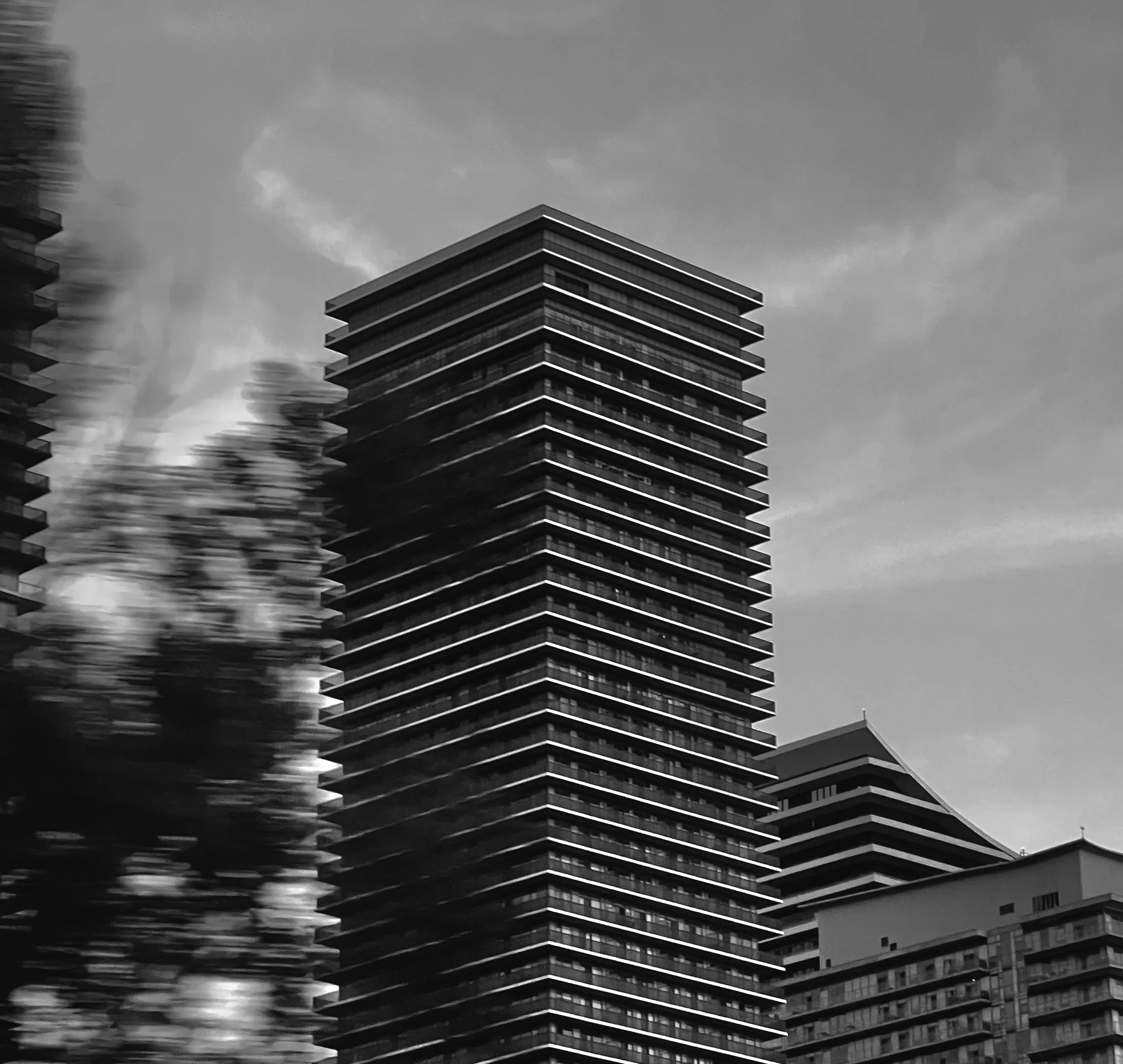 Black and white photo of modern high-rise buildings with horizontal lines and glass windows, against a cloudy sky.
