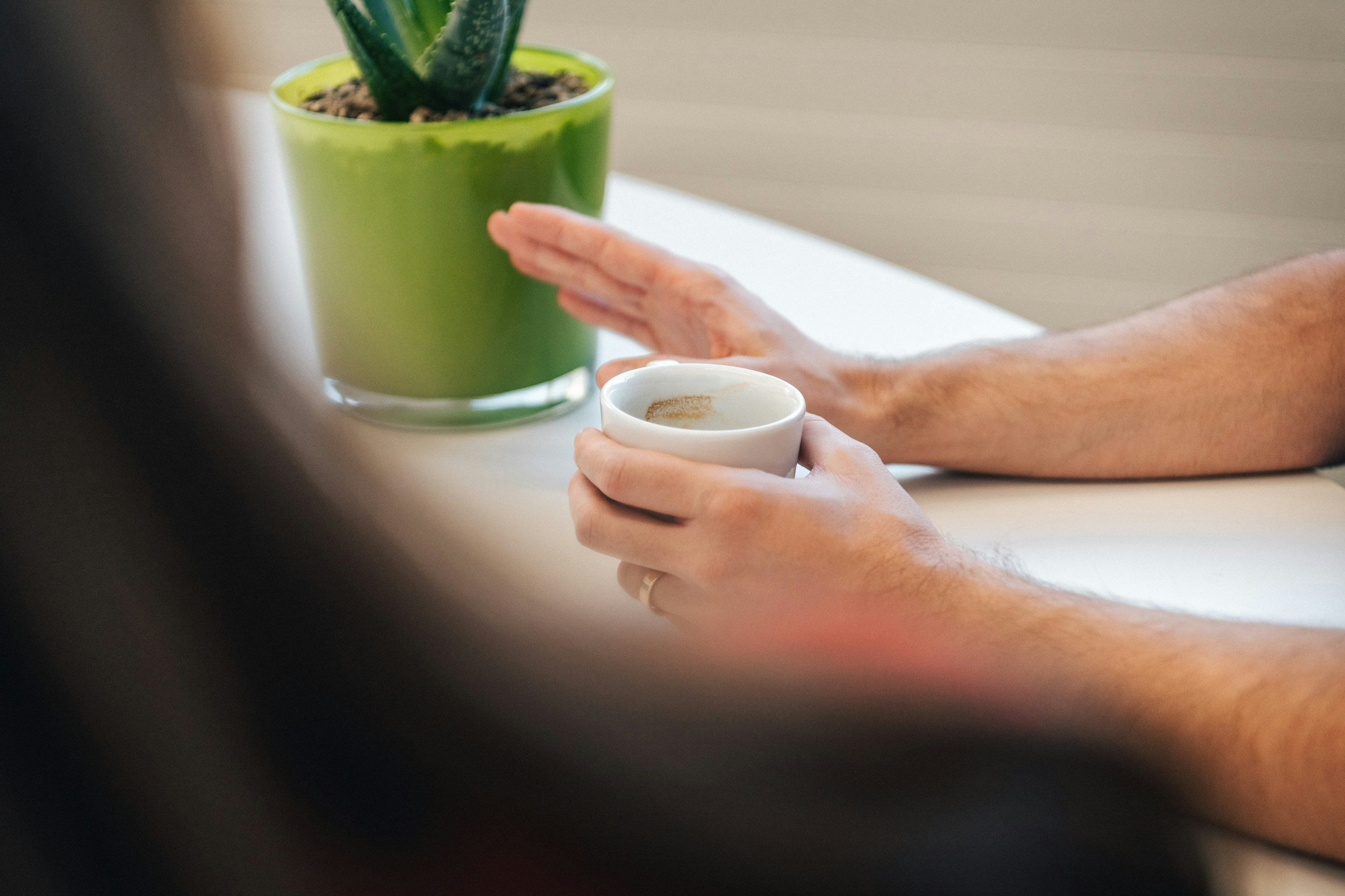 zoomed in shot of a green plant with a person's hand and a coffee cup