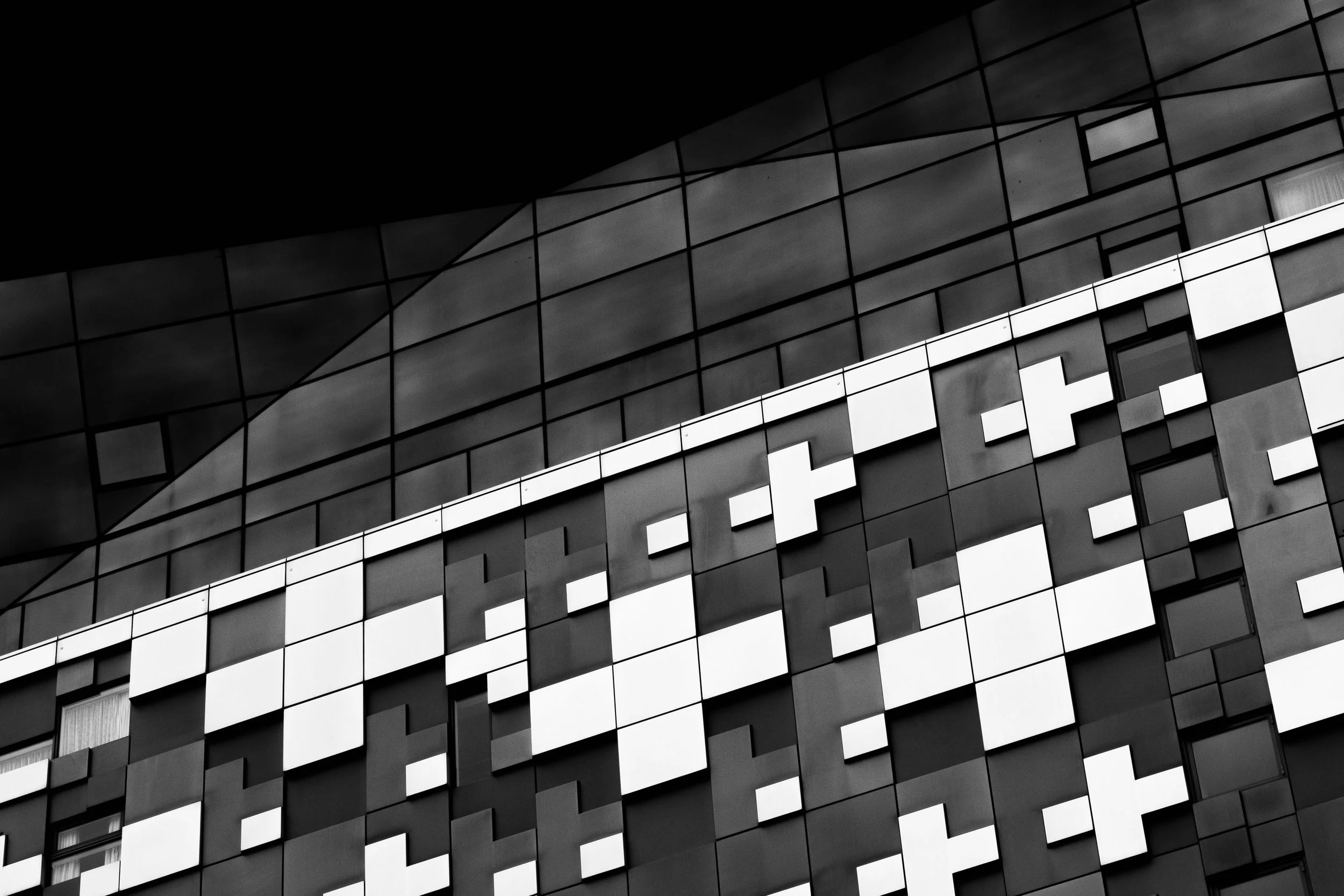 Black and white photo of a modern building with geometric patterns on its exterior, featuring various rectangular windows and panels.