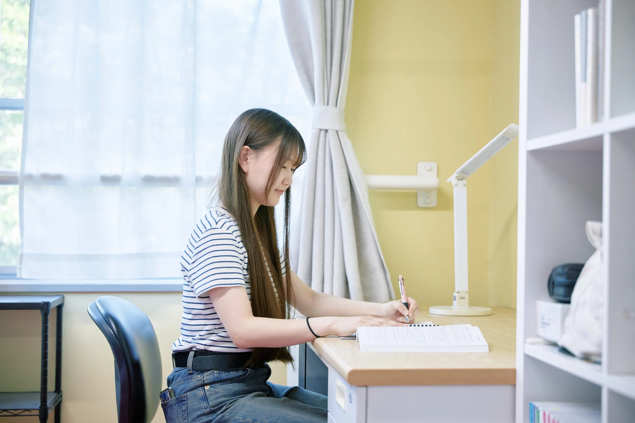 机の前でノートに書きながら勉強している若い女性