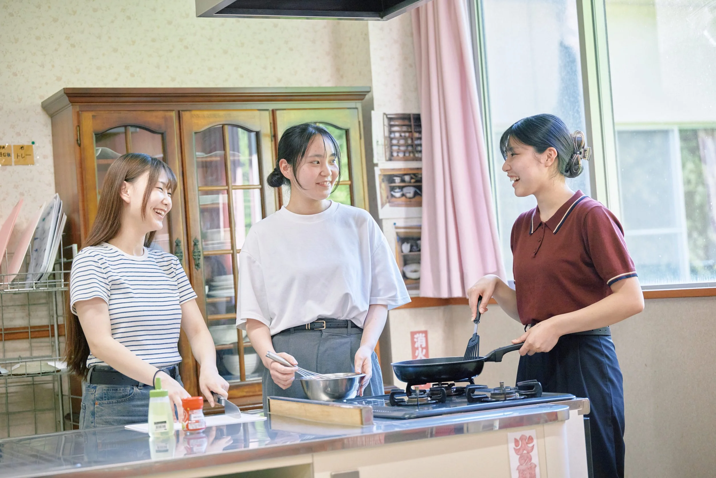 キッチンで3人の女性が料理をしながら会話している様子。