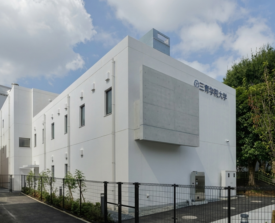 白い建物とフェンス、その側に樹木が見える。