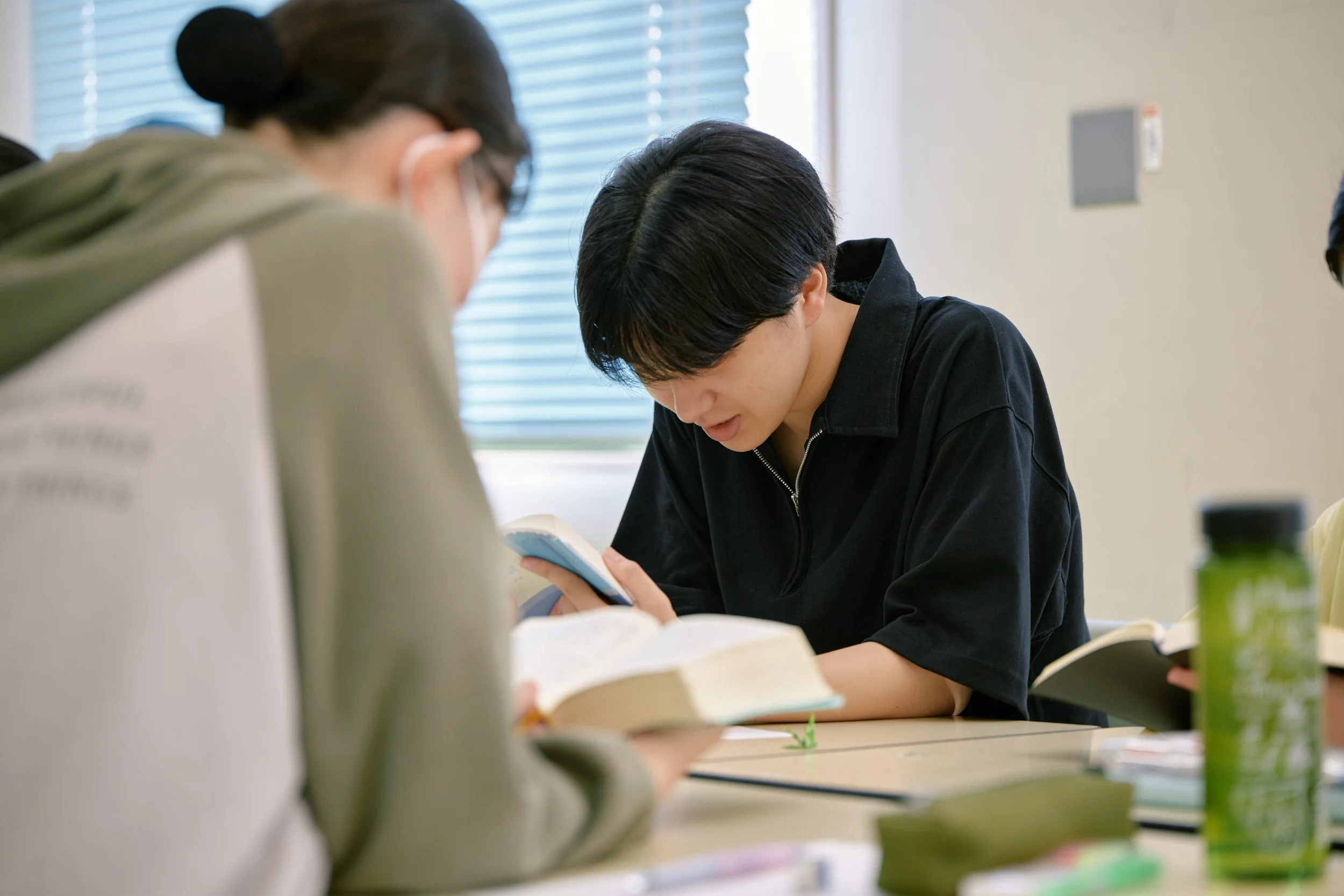 教室で勉強する学生たち。中央の少年が黒いシャツを着て、本を見ながら集中している。