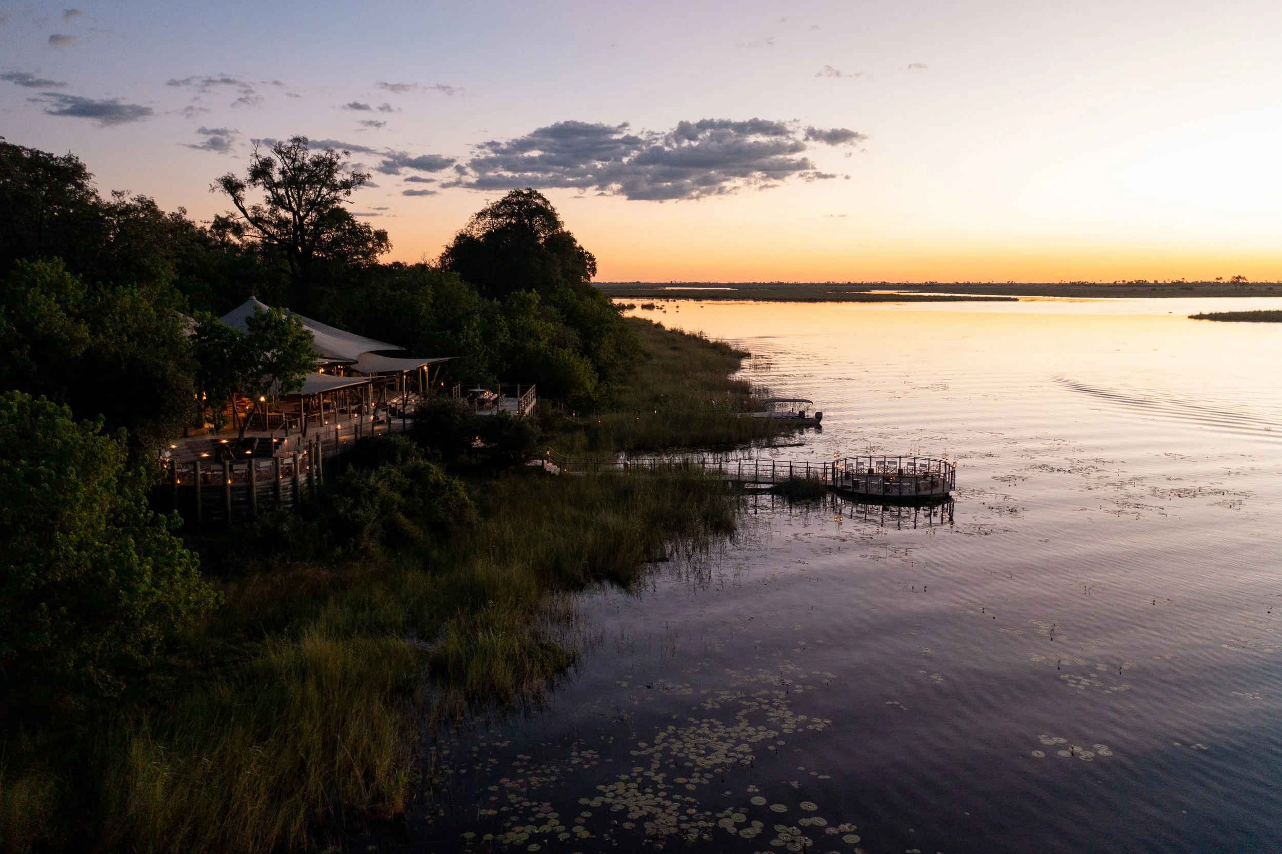 Sunset over a river with a canopy restaurant and boats docked along the shoreline.