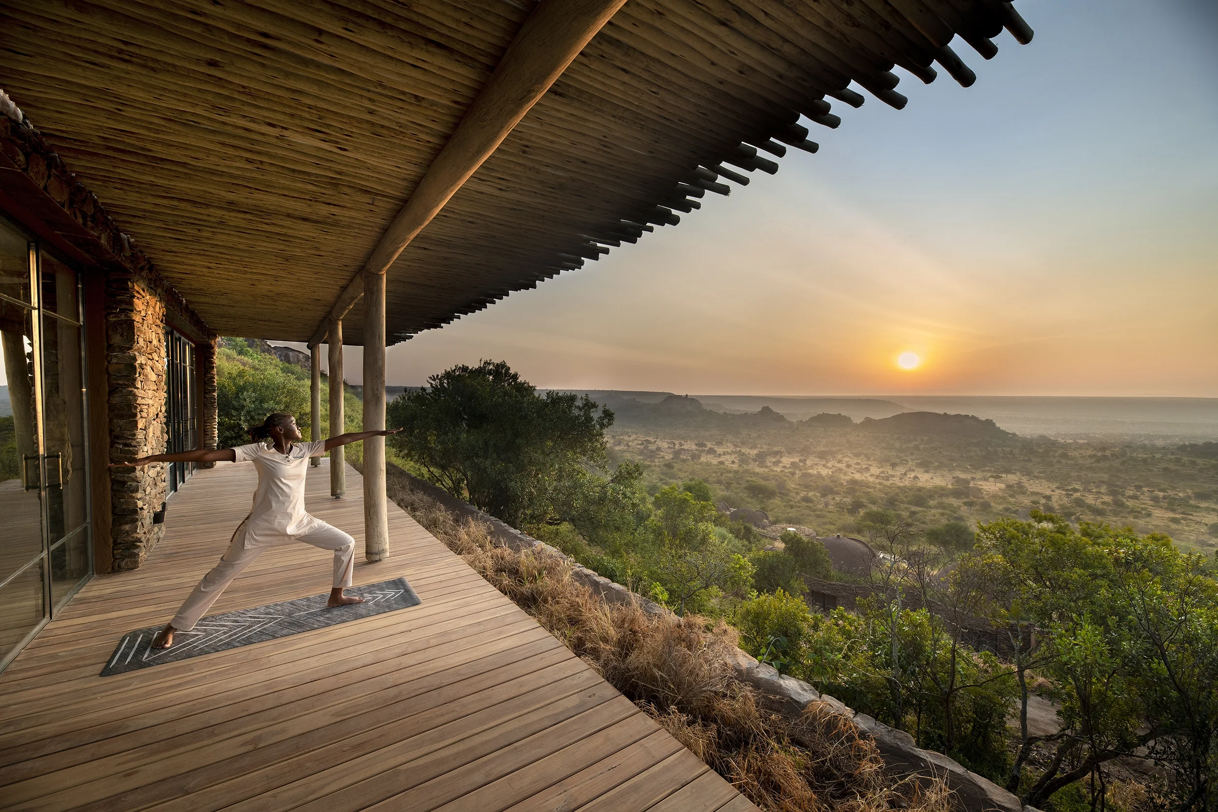 A woman practicing yoga on a wooden deck overlooking a scenic landscape during sunrise.