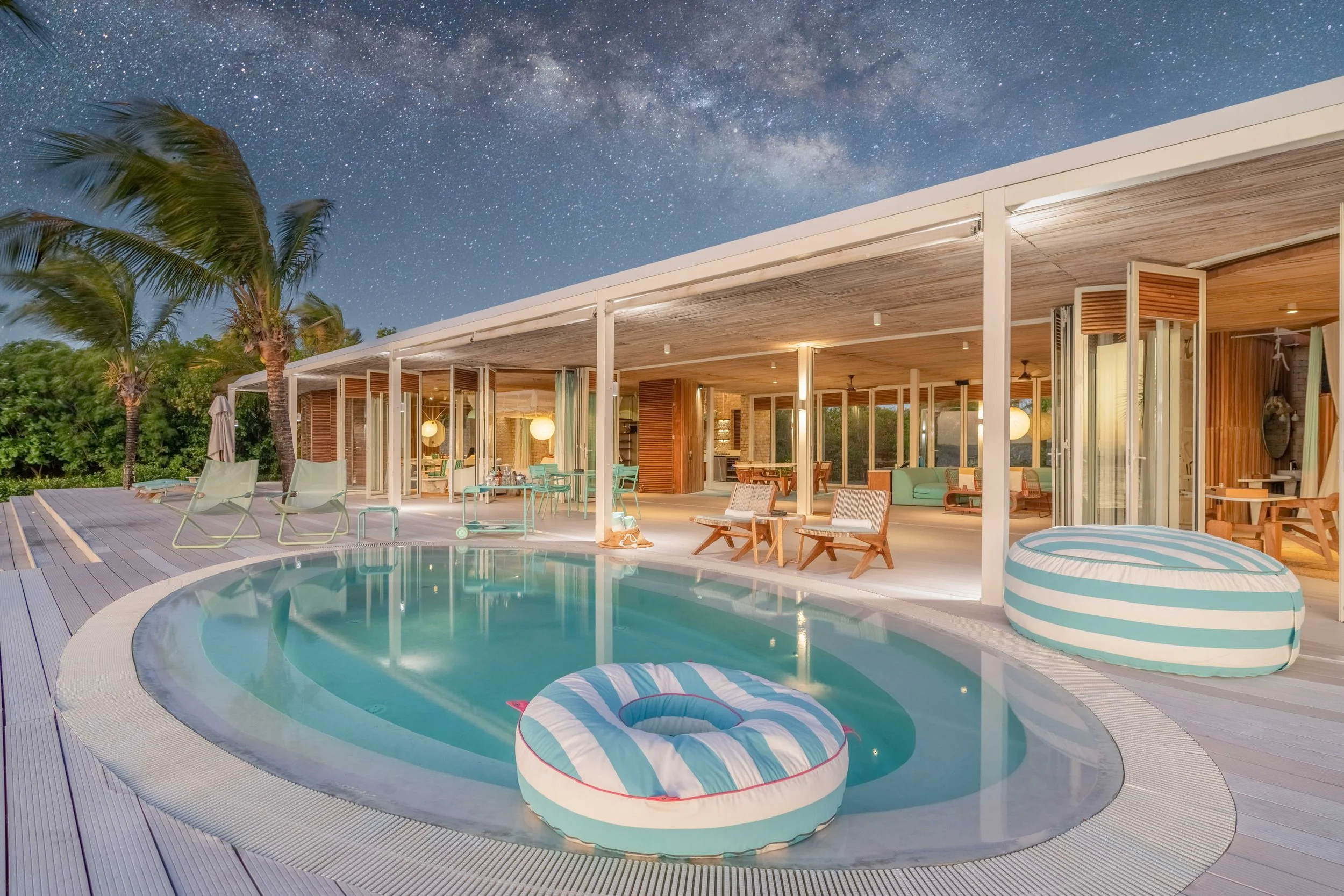 Luxury modern house with a swimming pool in the backyard, featuring outdoor seating and lounge chairs, under a starry night sky with the Milky Way visible.