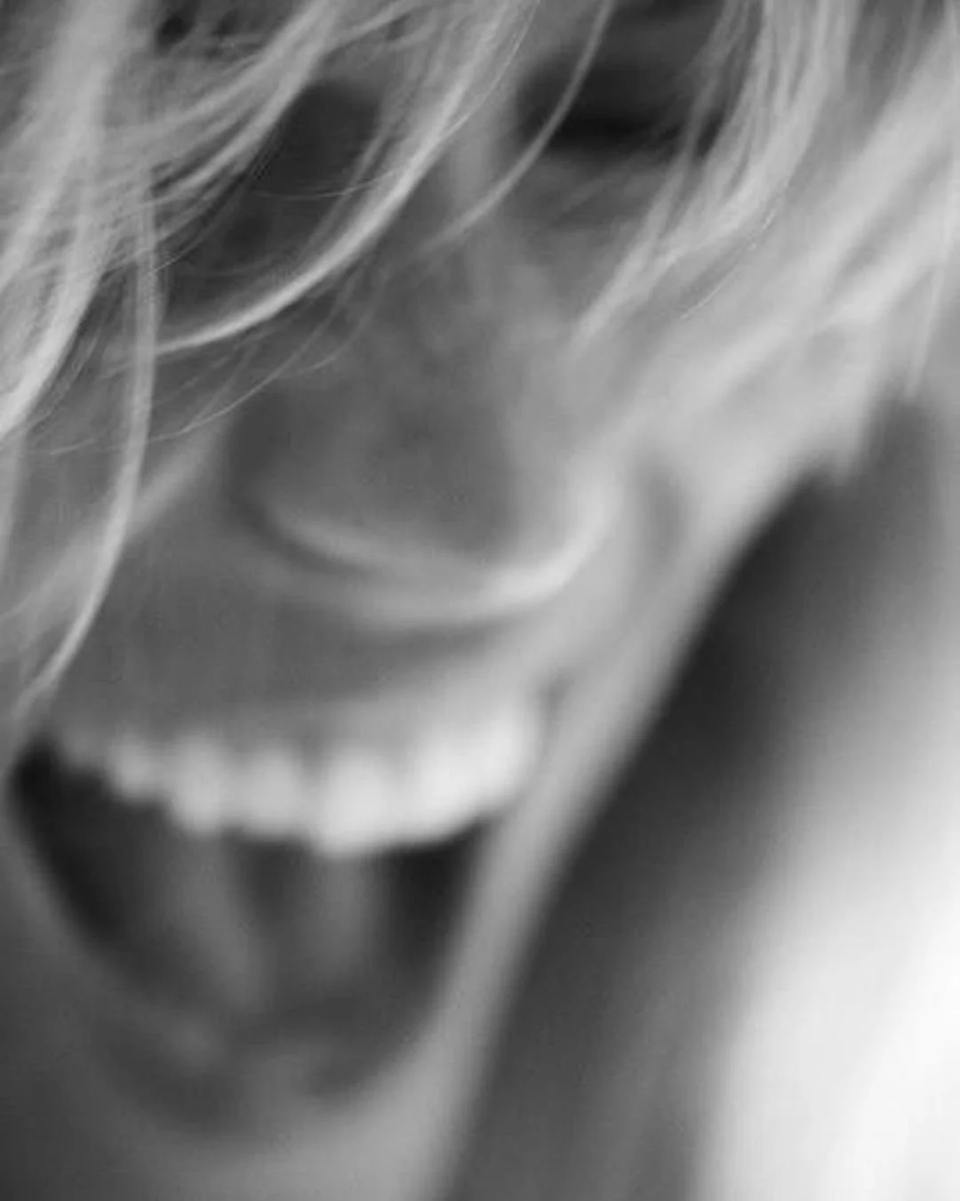 Nahaufnahme eines lachenden Kindes in Schwarz-Weiß, teilweise sichtbar mit lockigem Haar.