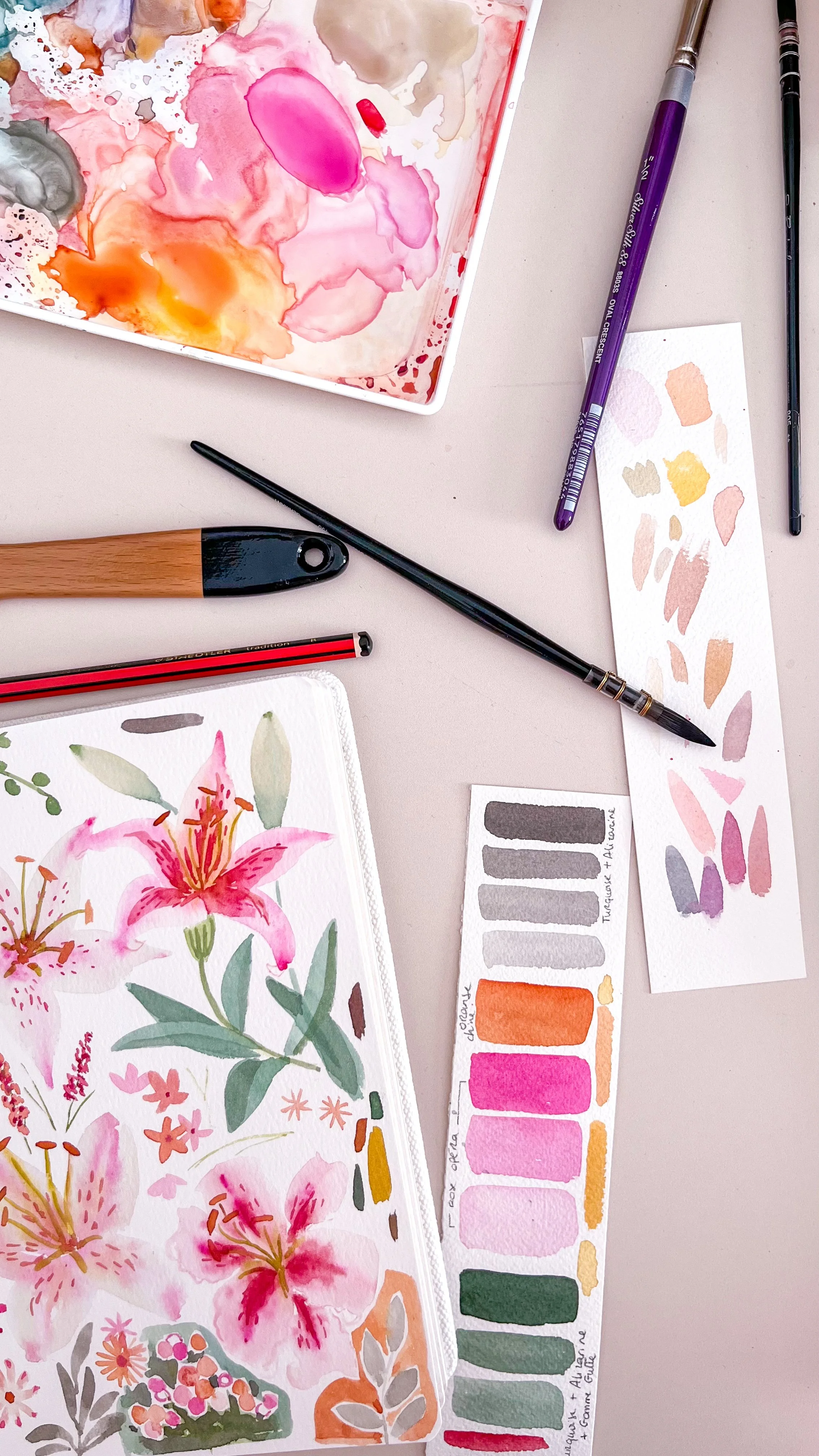 Matériel d'aquarelle comprenant des pinceaux, une palette avec des couleurs pastel, une peinture de fleurs en cours, et un carnet de croquis avec des motifs floraux en aquarelle.