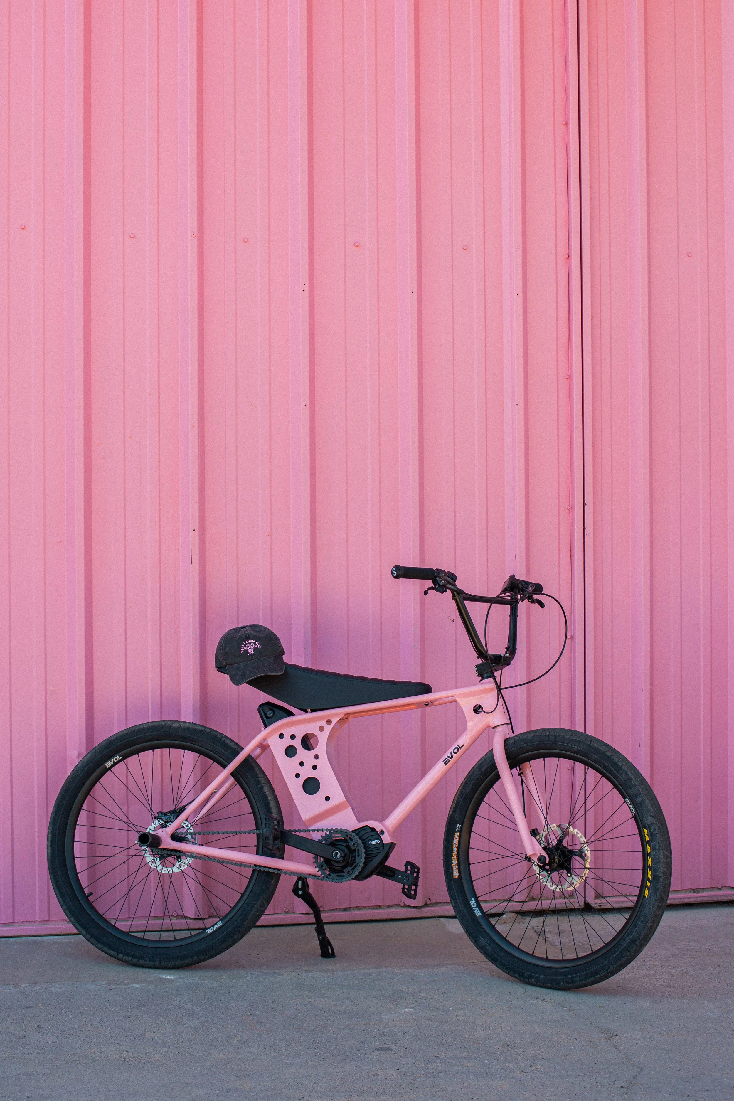 Collaboration avec EVOL, Vélo rose,  devant un mur en tôle rose dans la zone pédébert