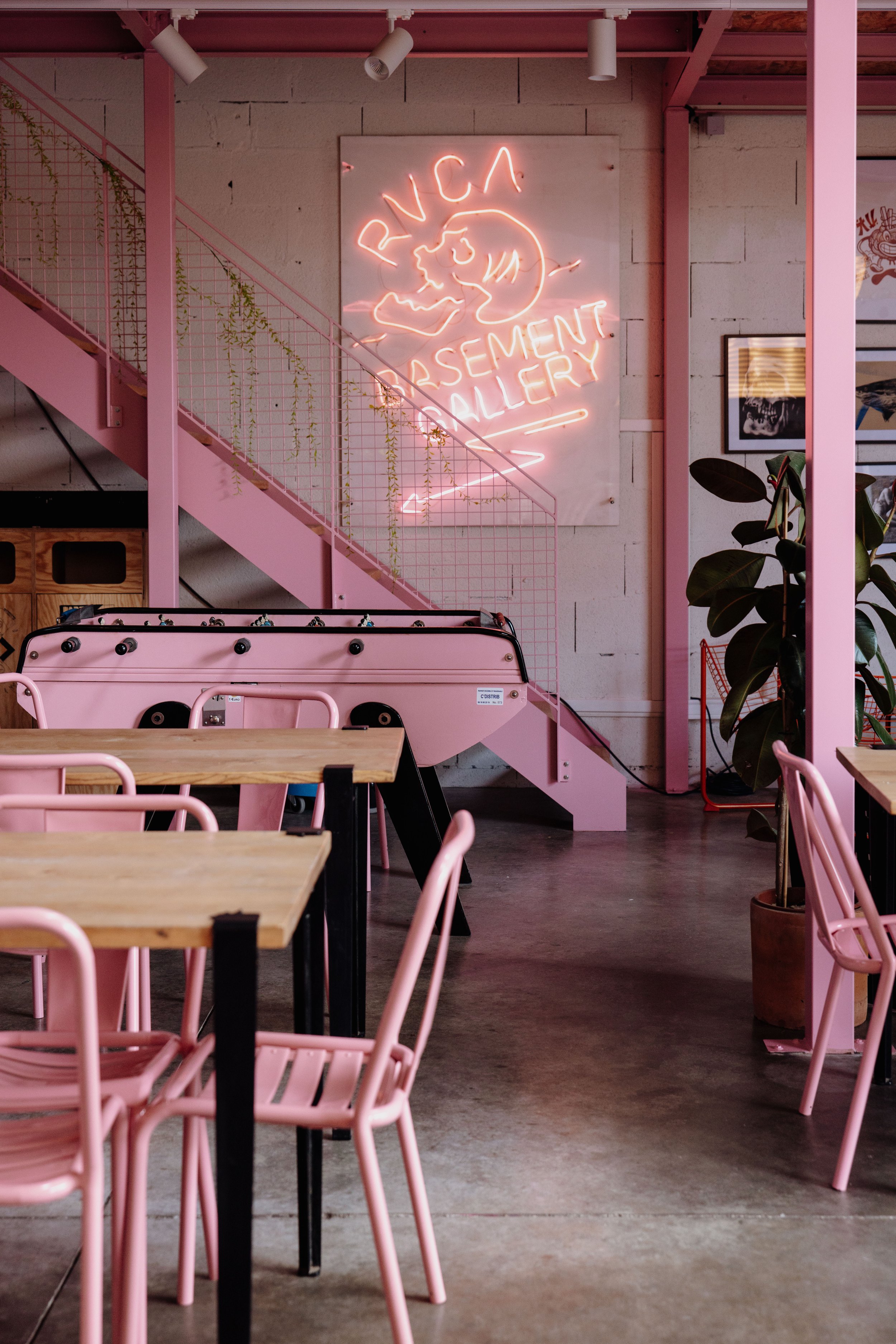 Intérieur Spot palace, avec des meubles en bois et chaises roses, une enseigne en néon rose indiquant 'RVA BASEMENT GALLERY'