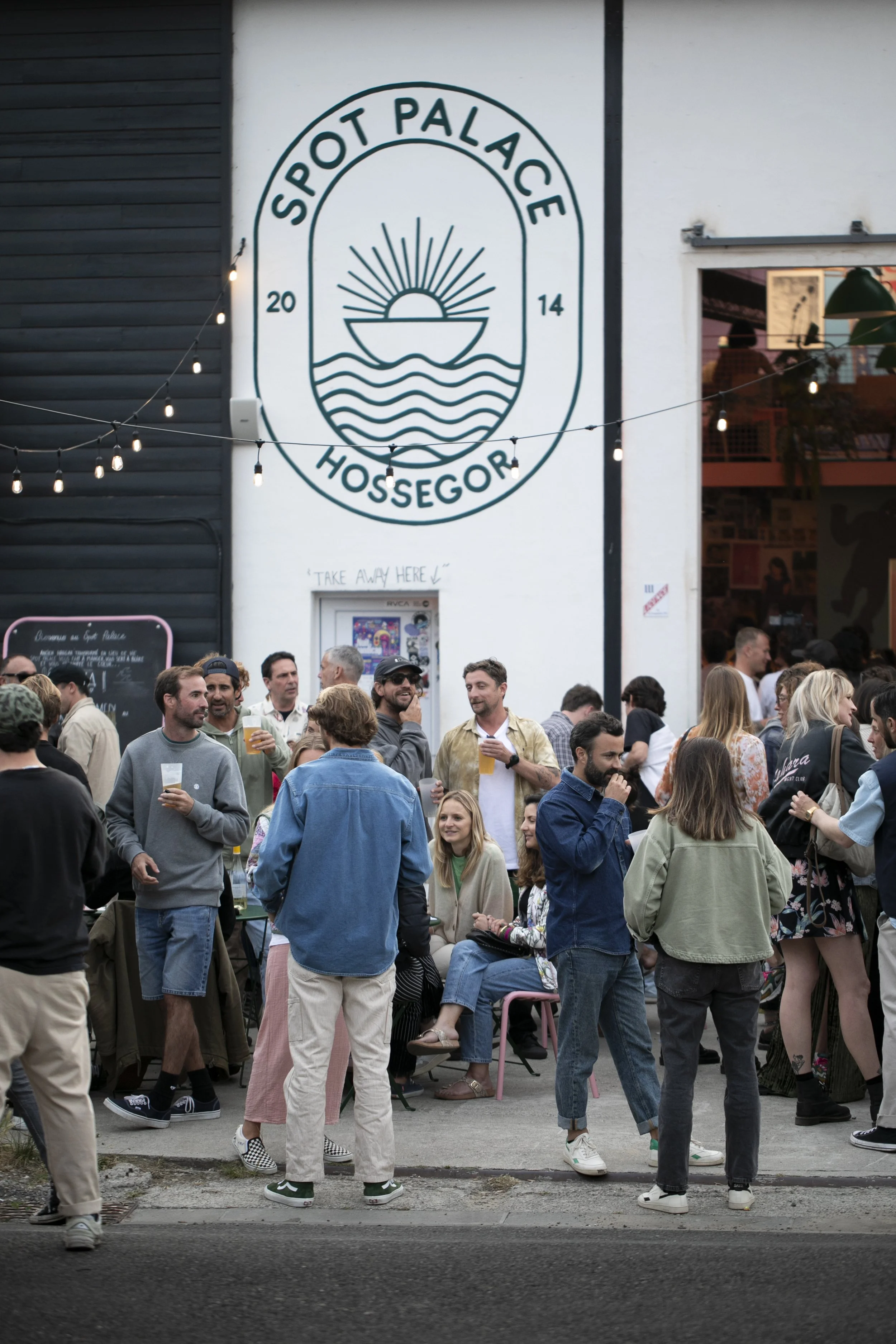 Un groupe de personnes à l'extérieur d'un bar ou restaurant en soirée, avec une enseigne portant le nom 'Spot Palace Hossegor' et une décoration lumineuse.