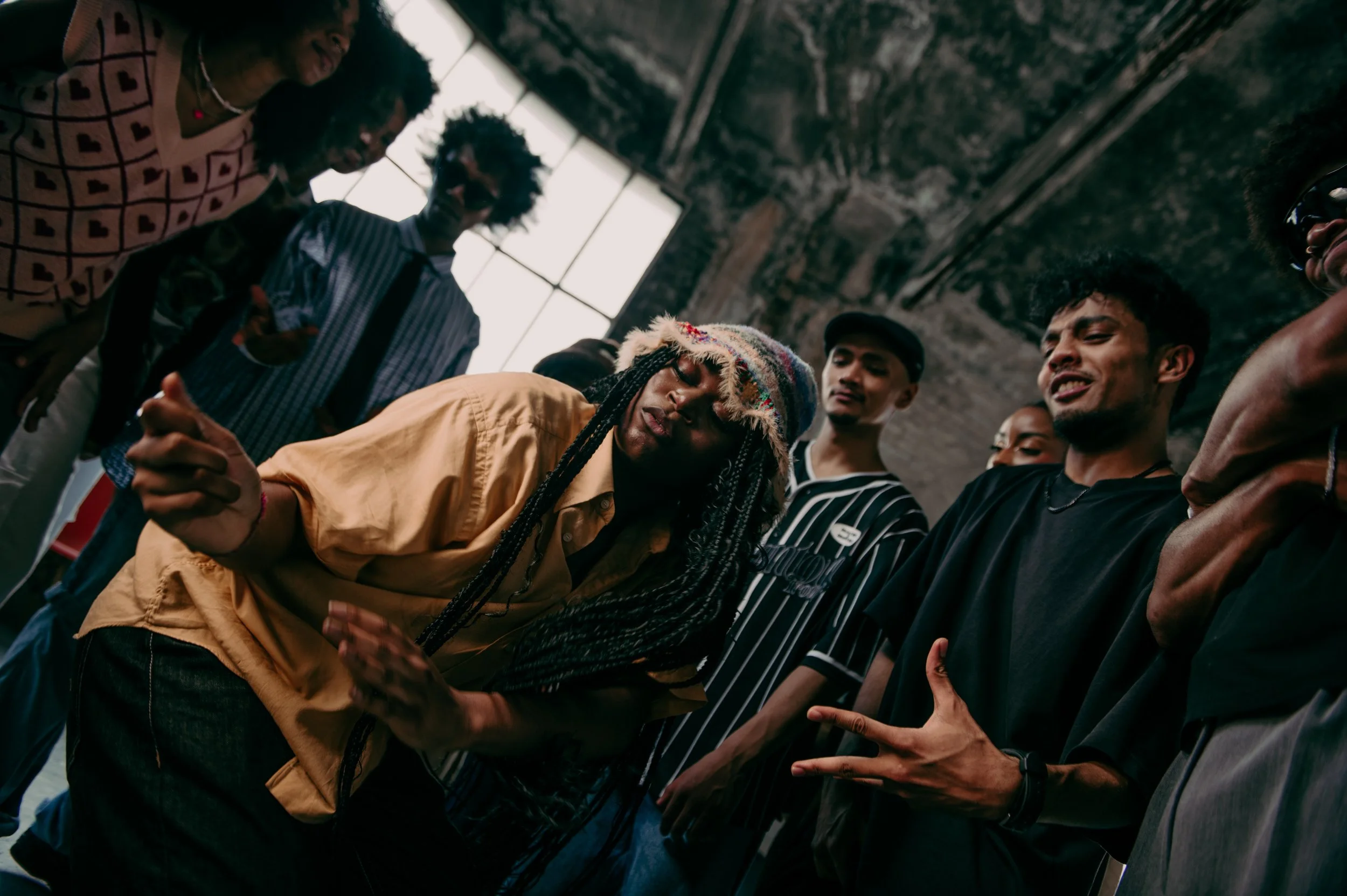 Groupe de jeunes en train de danser et d'apprécier une fête dans une ambiance décontractée dans un espace industriel avec de grandes fenêtres.