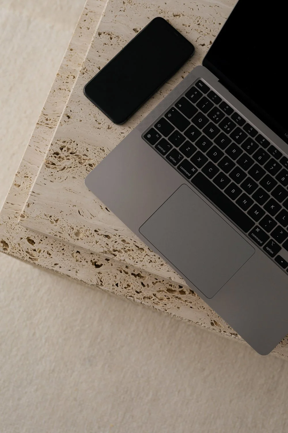 Laptop und Smartphone auf einem beigefarbenen Stein- oder Marmor-Tisch.