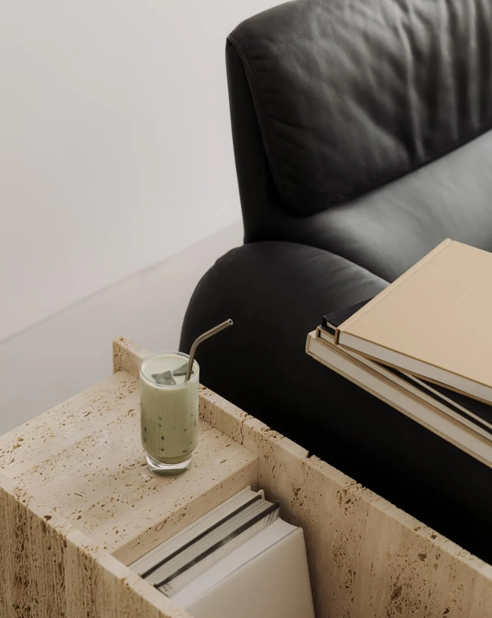 Schwarzes Ledersofa neben einem Beistelltisch mit einem Matcha Latte und mehreren Büchern.