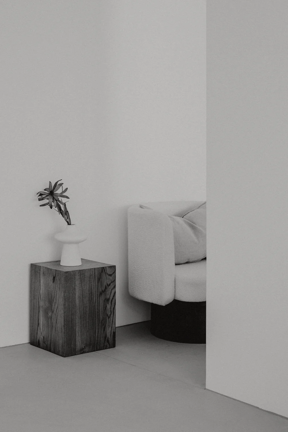 Ein minimalistisches Wohnzimmer mit weißen Wänden, einer eleganten weißen Couch, einem Holztisch mit einer Vase und einer Pflanze.