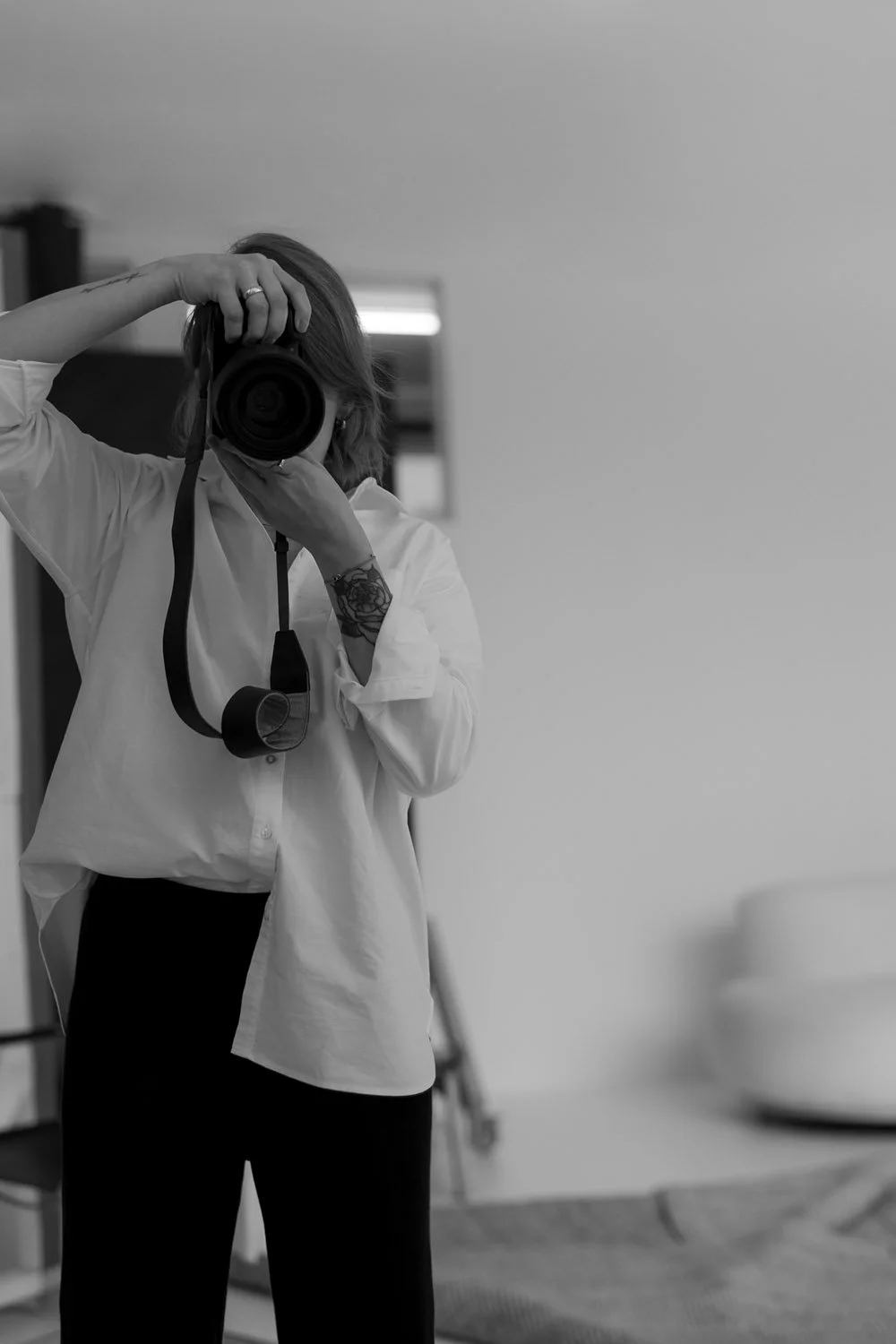 Frau mit Kamera in einem Raum fotografiert ihr Selbstbild in einem Spiegel, schwarz-weiß Fotografie