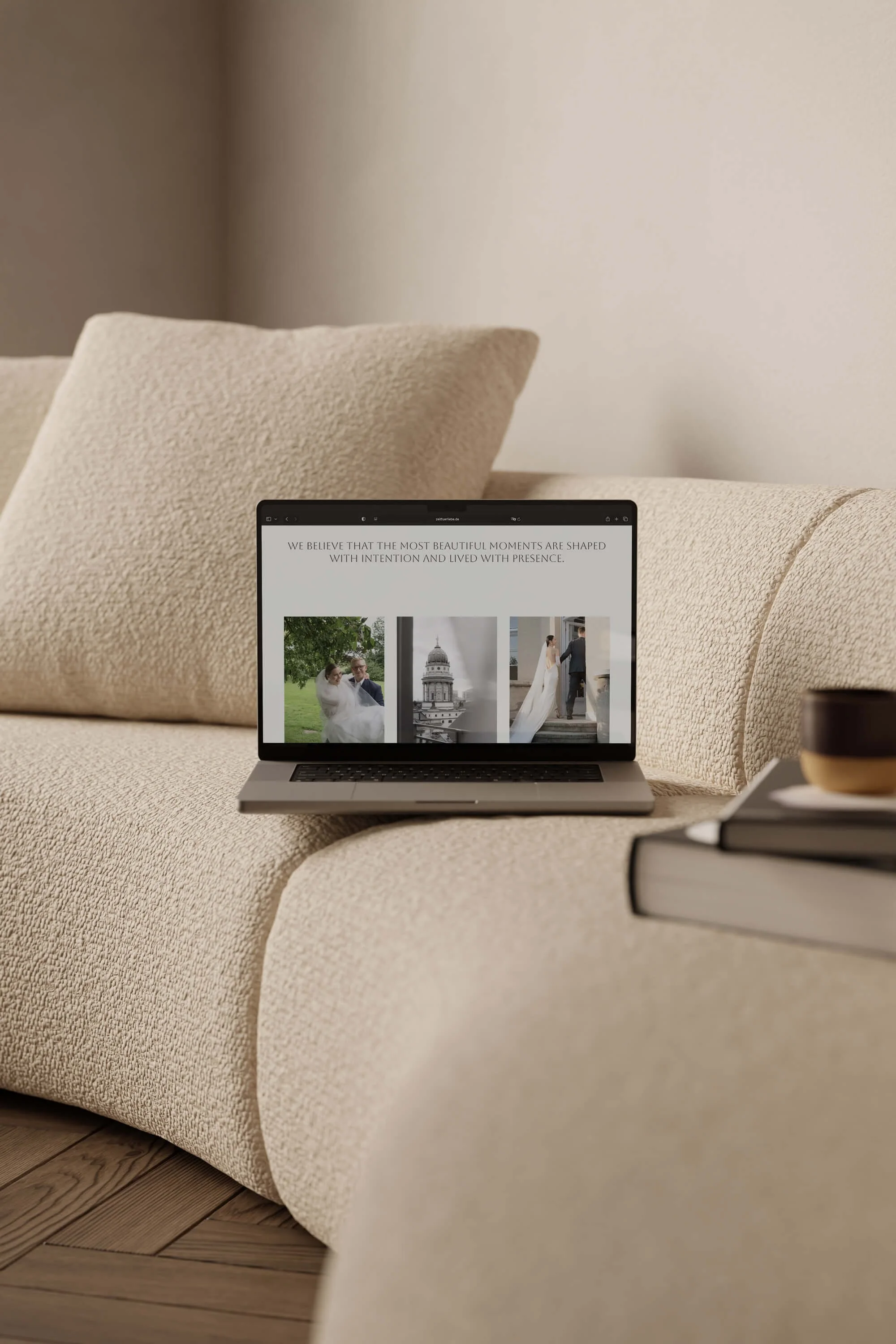 Ein offener Laptop auf einer beige Couch, der einen weißen Bildschirm mit Text zeigt, während im Vordergrund ein Buch liegt. Die Couch hat große Kissen, und der Boden ist aus Holz.