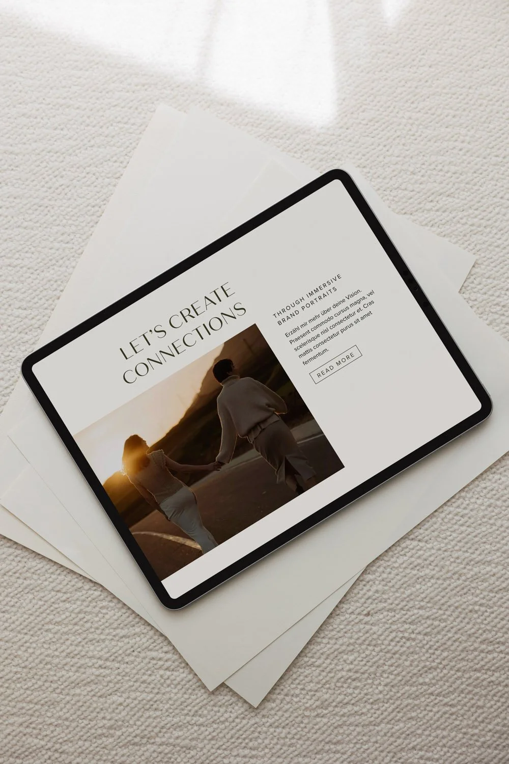Ein Tablet auf weißen Papieren zeigt eine Webseite mit dem Titel "Let's Create Connections" und einem Bild eines Paares, das sich an einem Sonnenuntergang hält, mit Text und einer Schaltfläche "Read More".