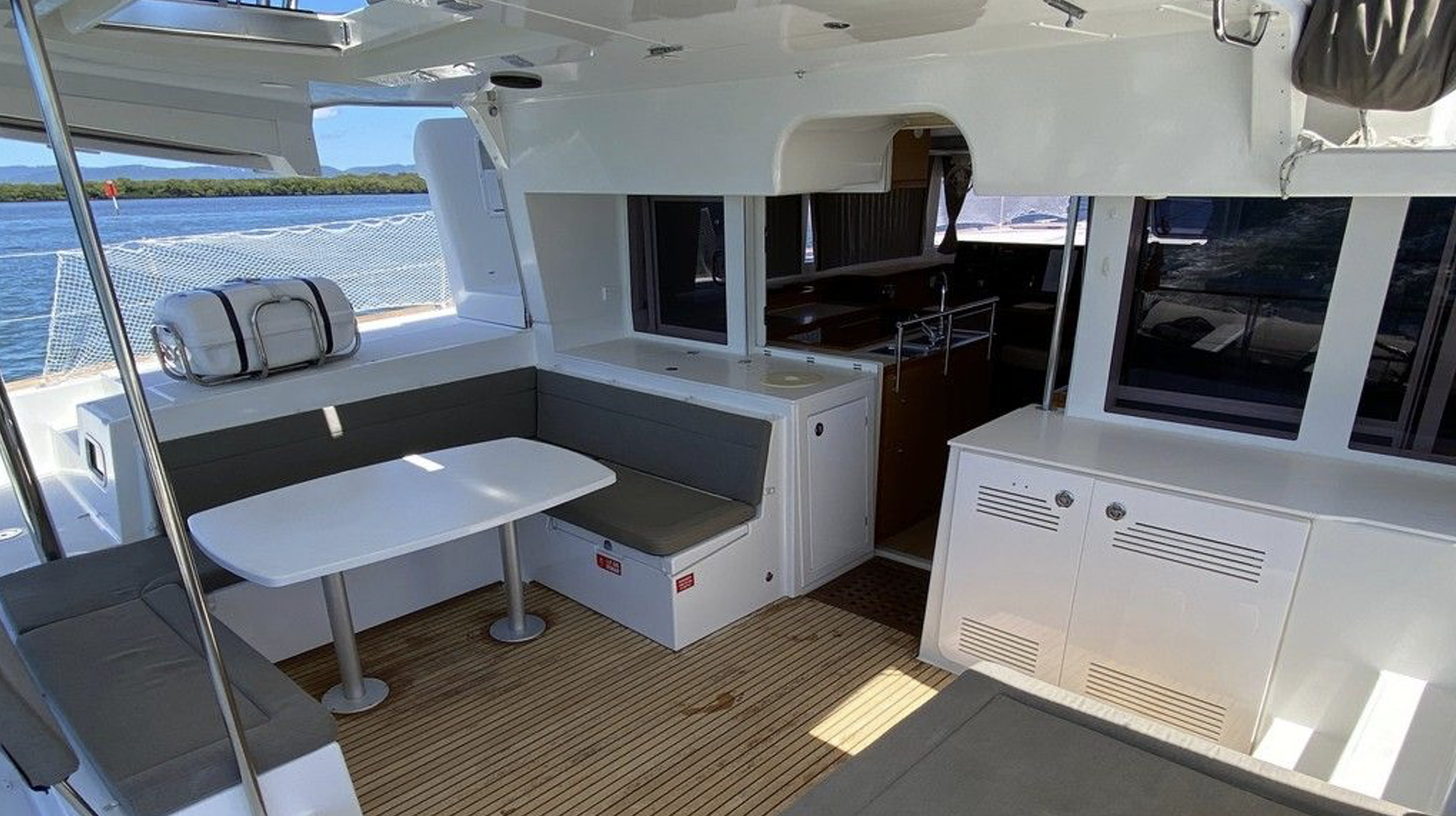 Innenansicht eines Segelschiffs mit Sitzgruppe, Fernseher und Blick auf das Meer im Hintergrund.