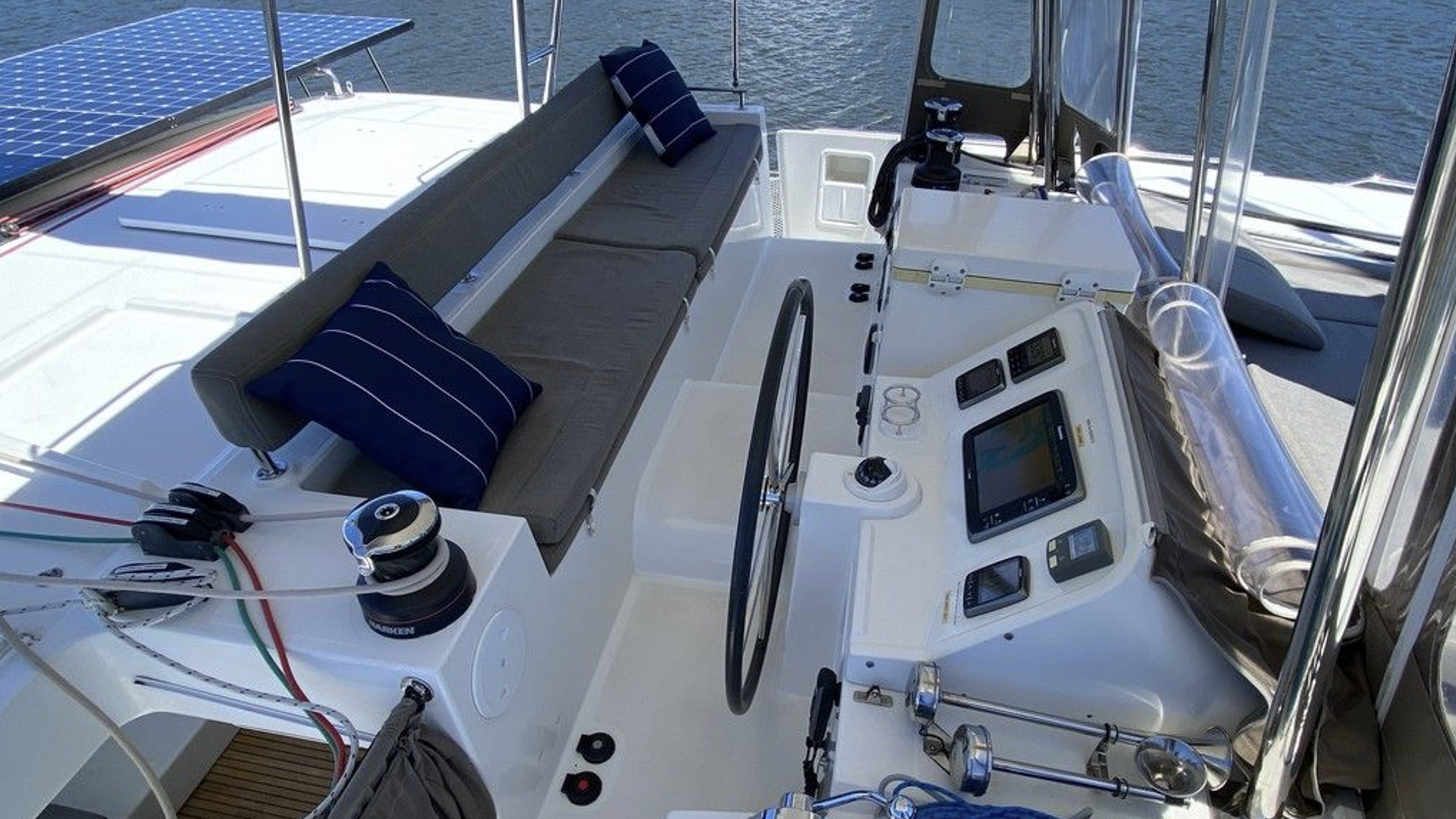 Die Steuerkabine eines Segelboots mit Instrumenten, Steuerrad, Sitzen, Kissen und einem Sonnenkollektor auf dem Dach.