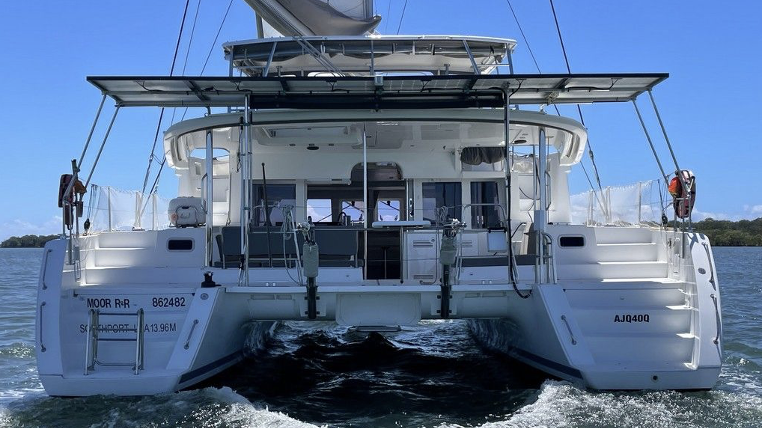 Ansicht eines weißen Segelboots auf dem Wasser, Blick von hinten, mit Segel und Kiel im Vordergrund, klares blaues Himmel im Hintergrund.