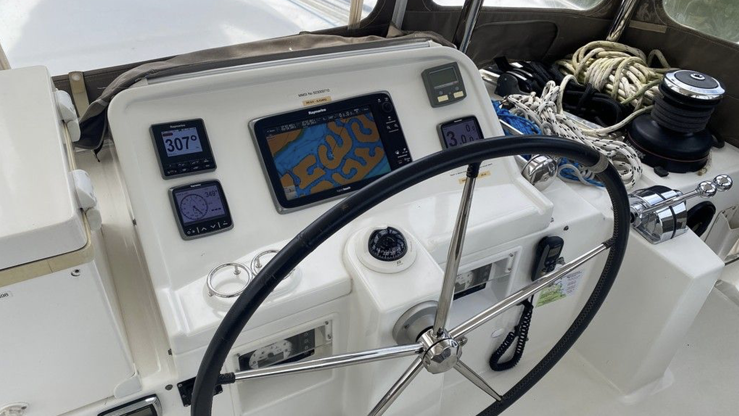 Steuerstand eines Segelboots mit Navigations- und Instrumentenbildschirm, Steuerknüppel, Ruder, und Tauwerk.