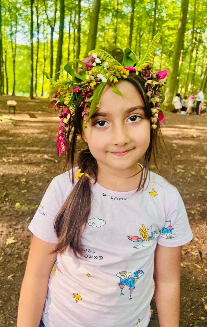 Young girl with a flower crown made of various flowers and green leaves, standing in a forest.