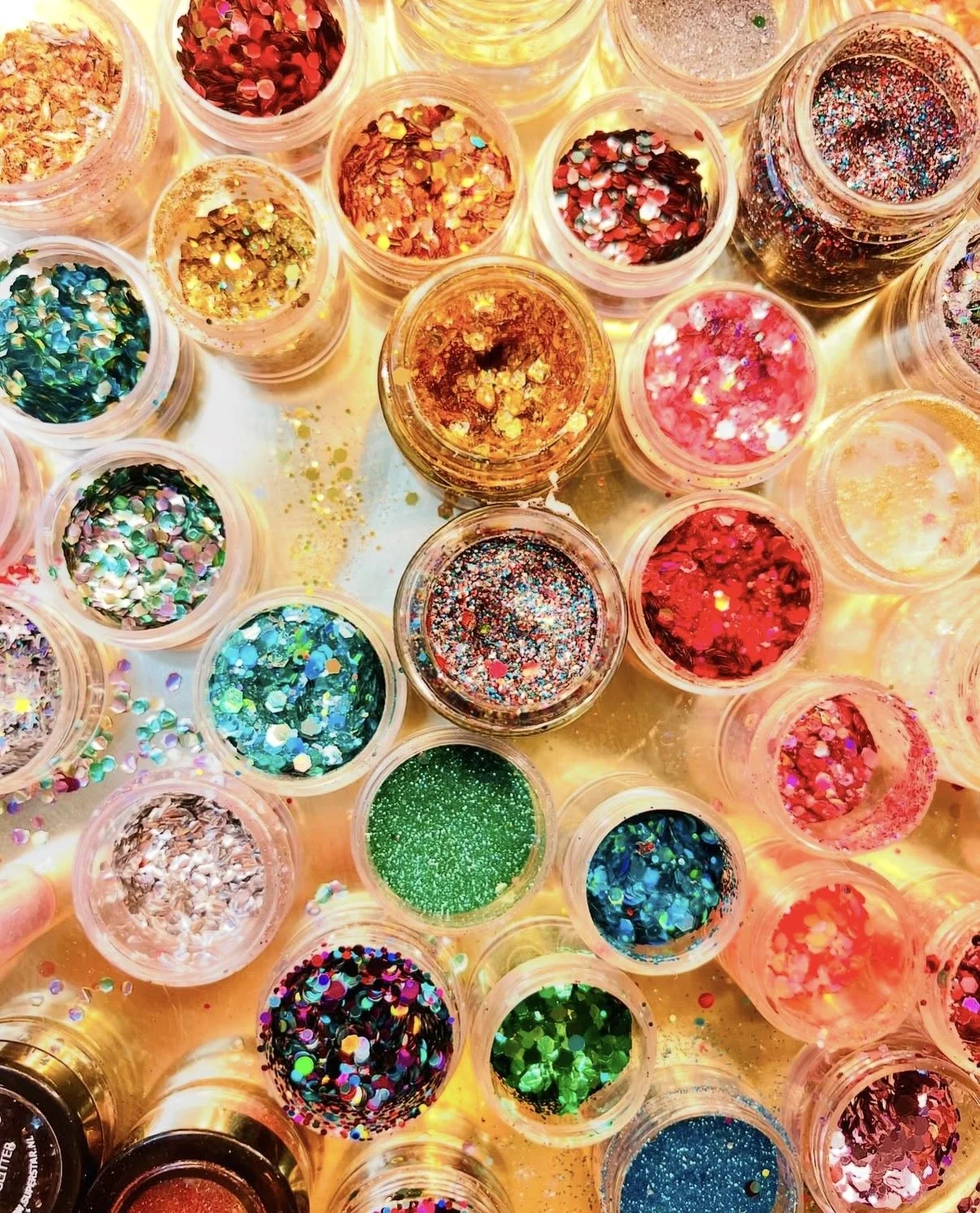 Close-up of multiple small containers filled with colorful glitter, arranged on a bright surface.