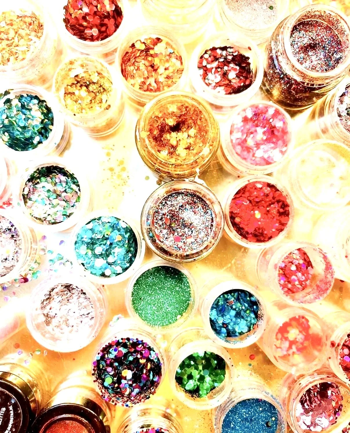 Small containers filled with colorful glitter and confetti, arranged closely together on a surface.