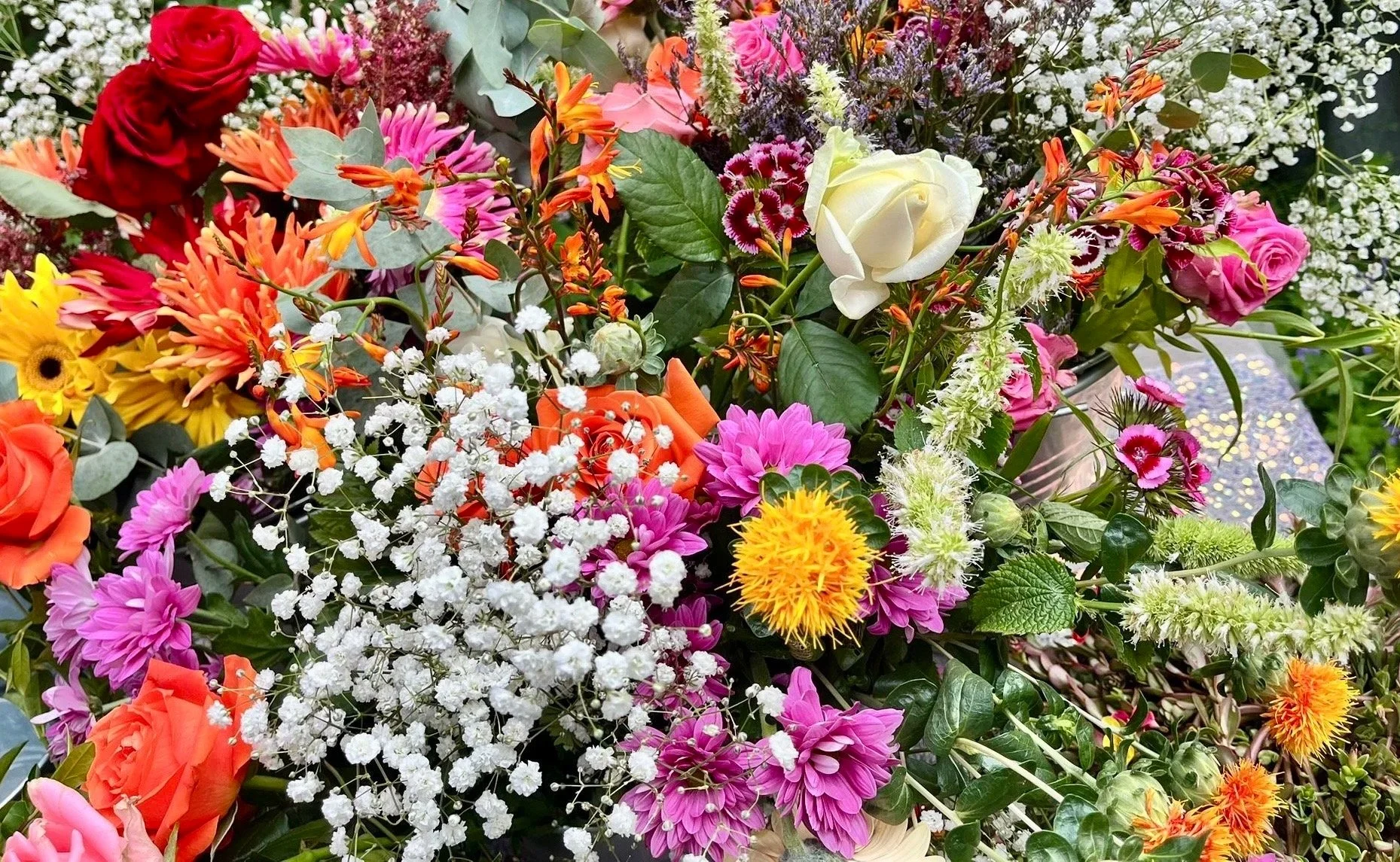 A vibrant bouquet of various colorful flowers including roses, sunflowers, dahlias, baby's breath, and assorted greenery.