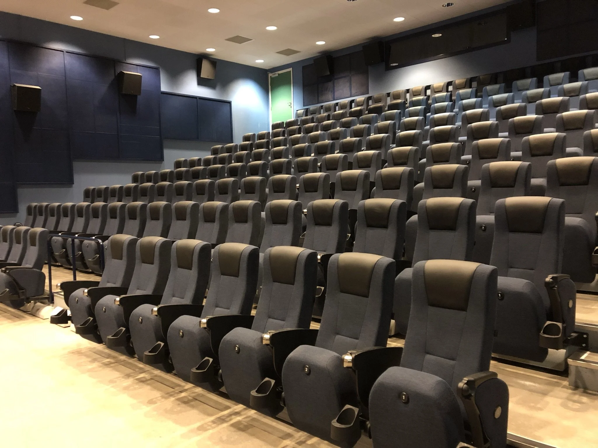 En tom kinokjø som har flere rader med komfortable, grå filmerstoler med svarte armlener, på en teaterrampe under et tak med spotlights.