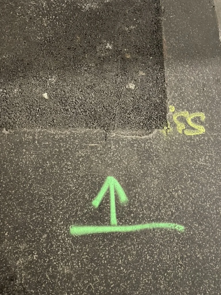 Green chalk arrow pointing upward on pavement, with yellow markings nearby.