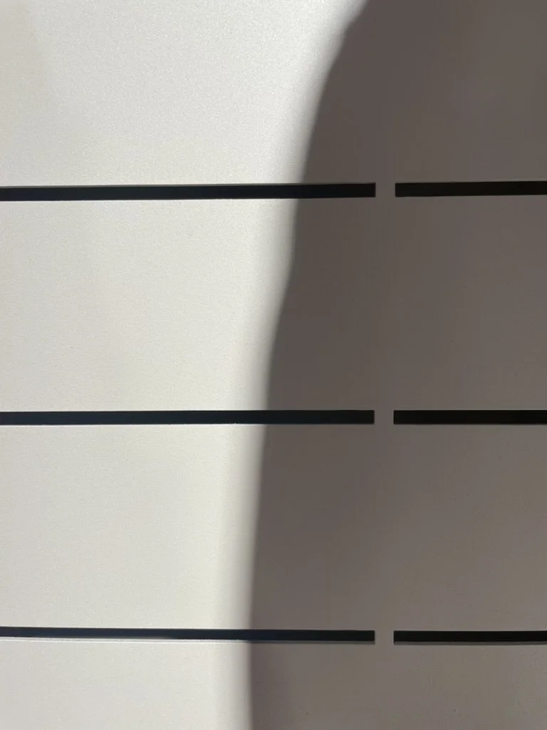Close-up of a white surface with black horizontal lines, partially covered by a shadow.