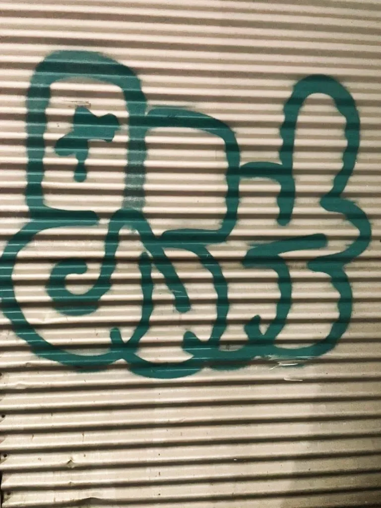 Graffiti of a butterfly drawn with teal-colored spray paint on a corrugated metal surface.