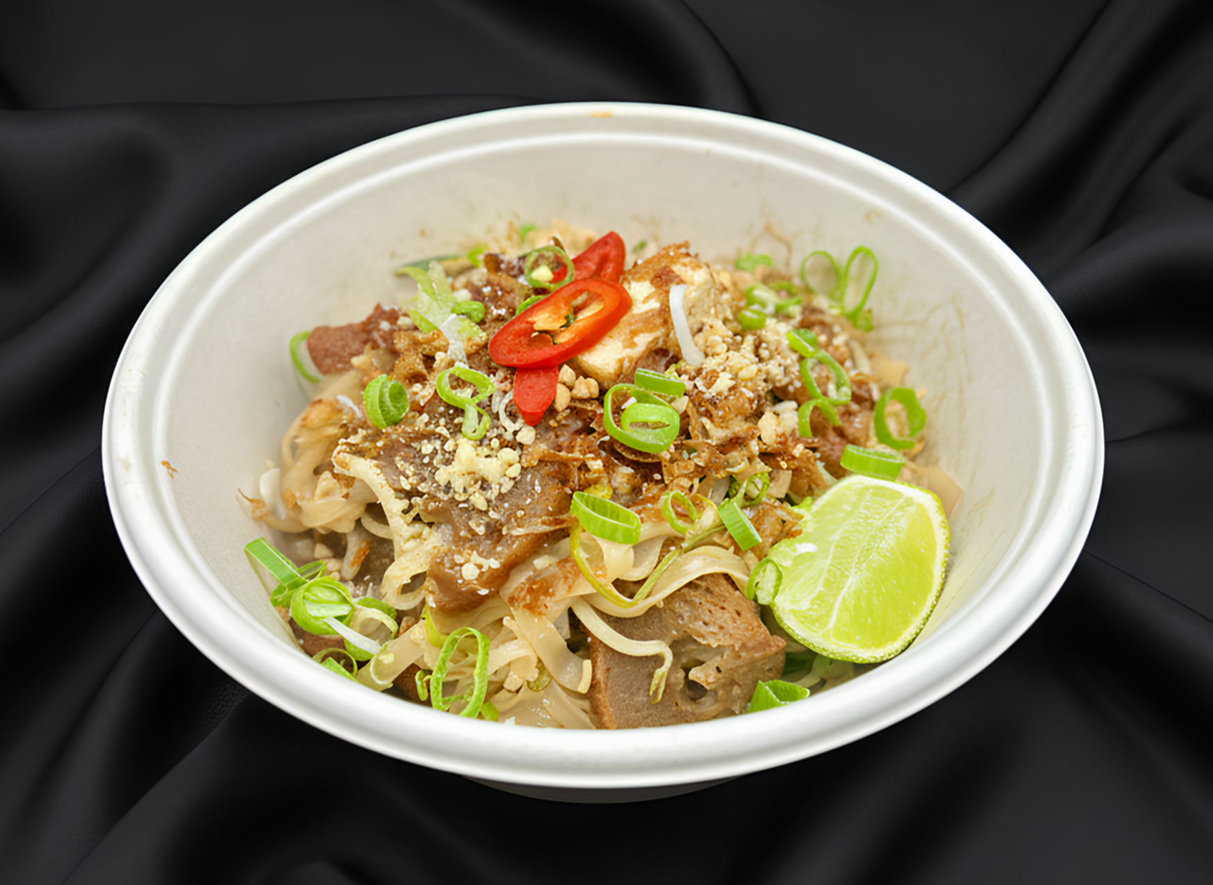 A bowl of noodles, meat, green onions, chili, lemon, and spices, looks like an Asian dish.