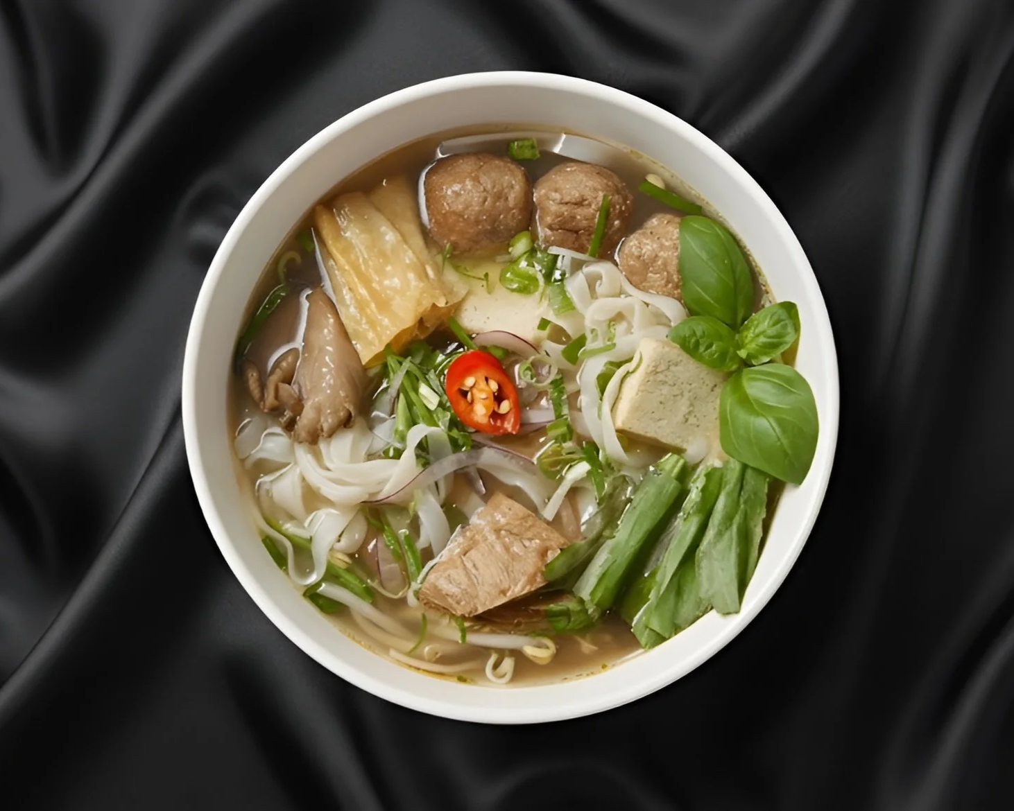 A bowl of Vietnamese Pho with vegan meatballs, vegan plant-based meat, rice noodles, vegetables, chili, basil and tofu.