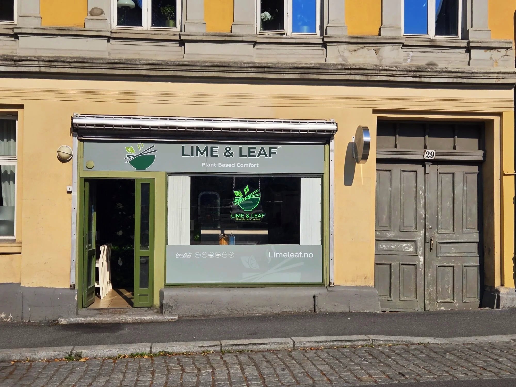En butikkfront for Lime & Leaf, et plantebasert matsted. Skiltet viser logo med en bolle og spisepinner, og teksten 'Plant-Based Comfort'.