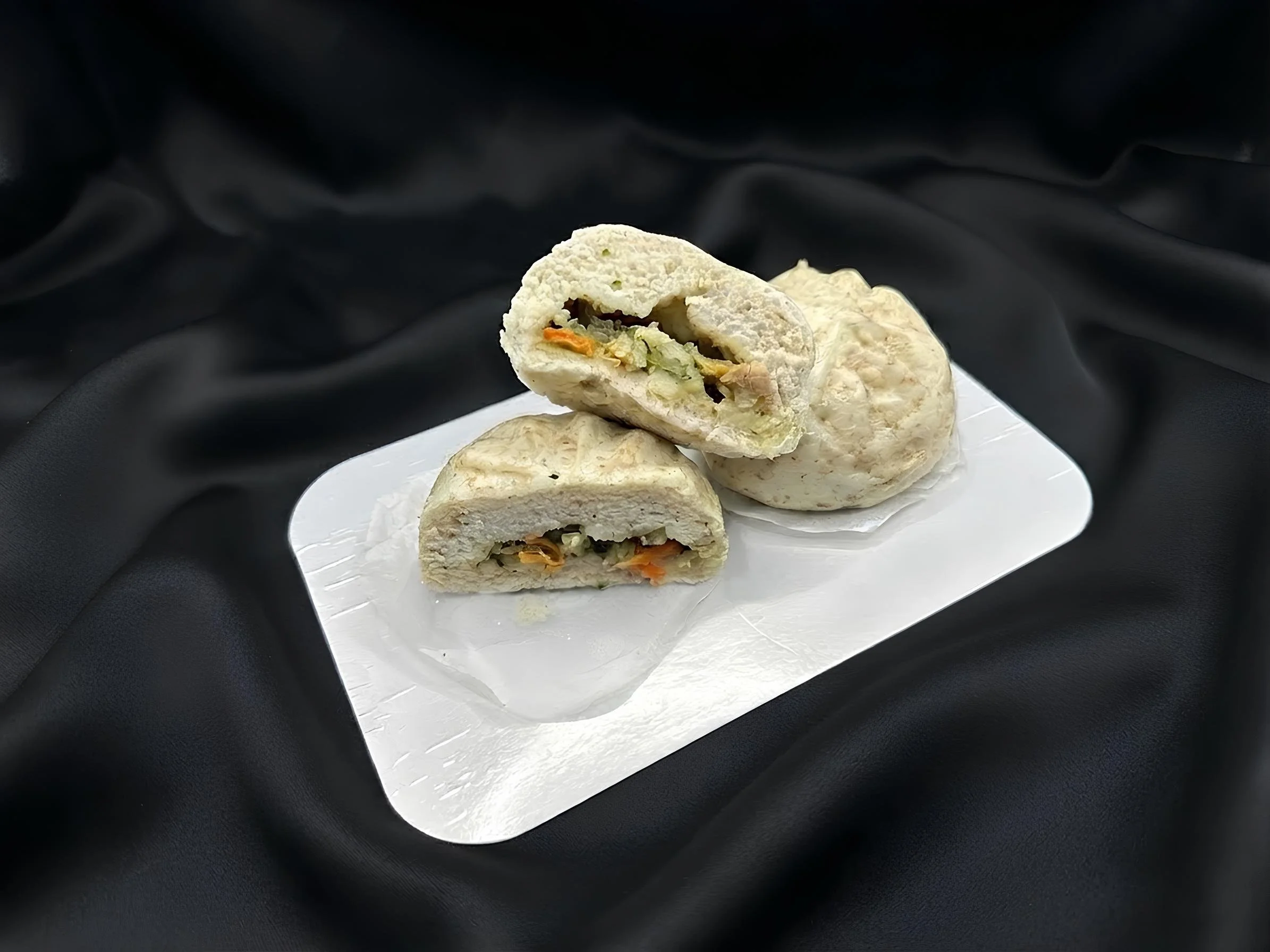 Kuttformet sandwich med fyll som grønnsaker og kjøtt, servert på en hvit tallerken med papirunderlag.