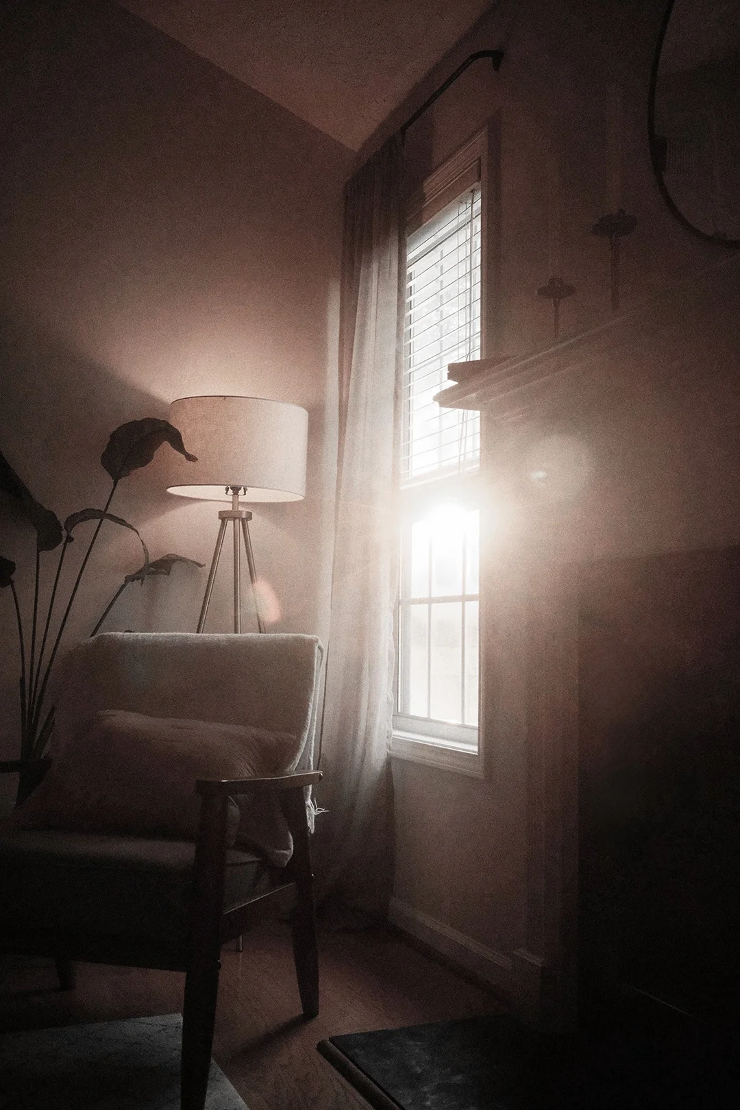 Sunlight streams through a window, illuminating a room with a tall floor lamp, white armchair, and light-colored curtains.