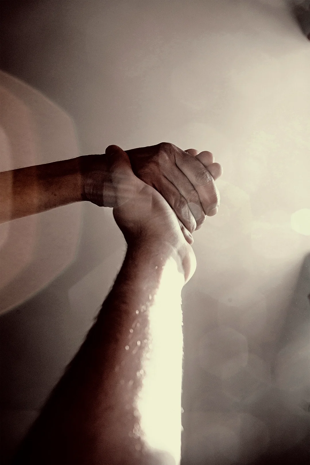Two hands clasped together in a handshake or grasp, illuminated by soft, natural light.