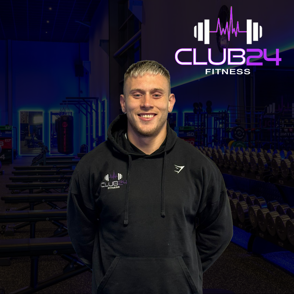 A young man smiling in a gym with gym equipment and a sign that says CLUB24 FITNESS.