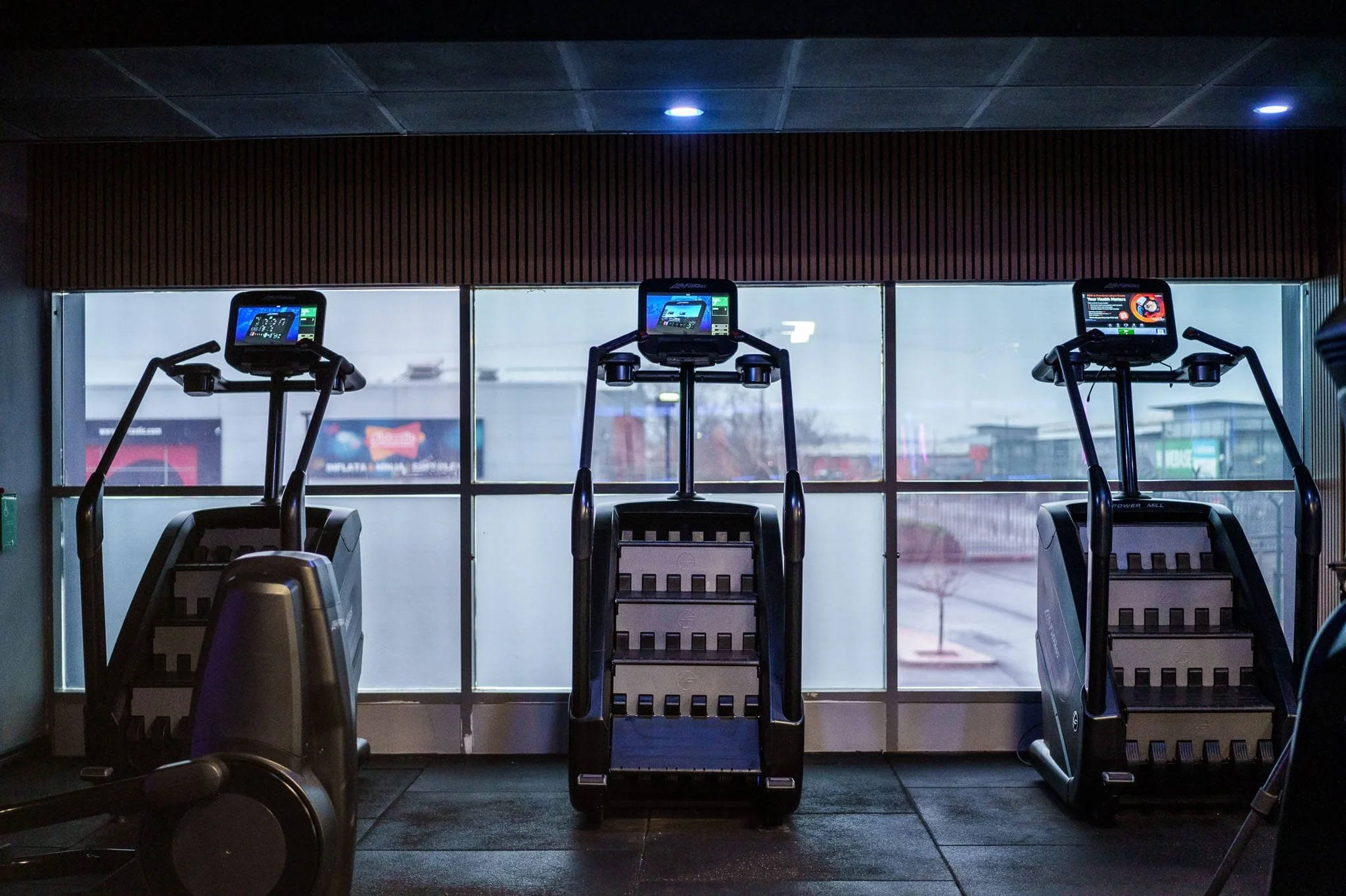 Three ellipticals in a gym facing large windows.