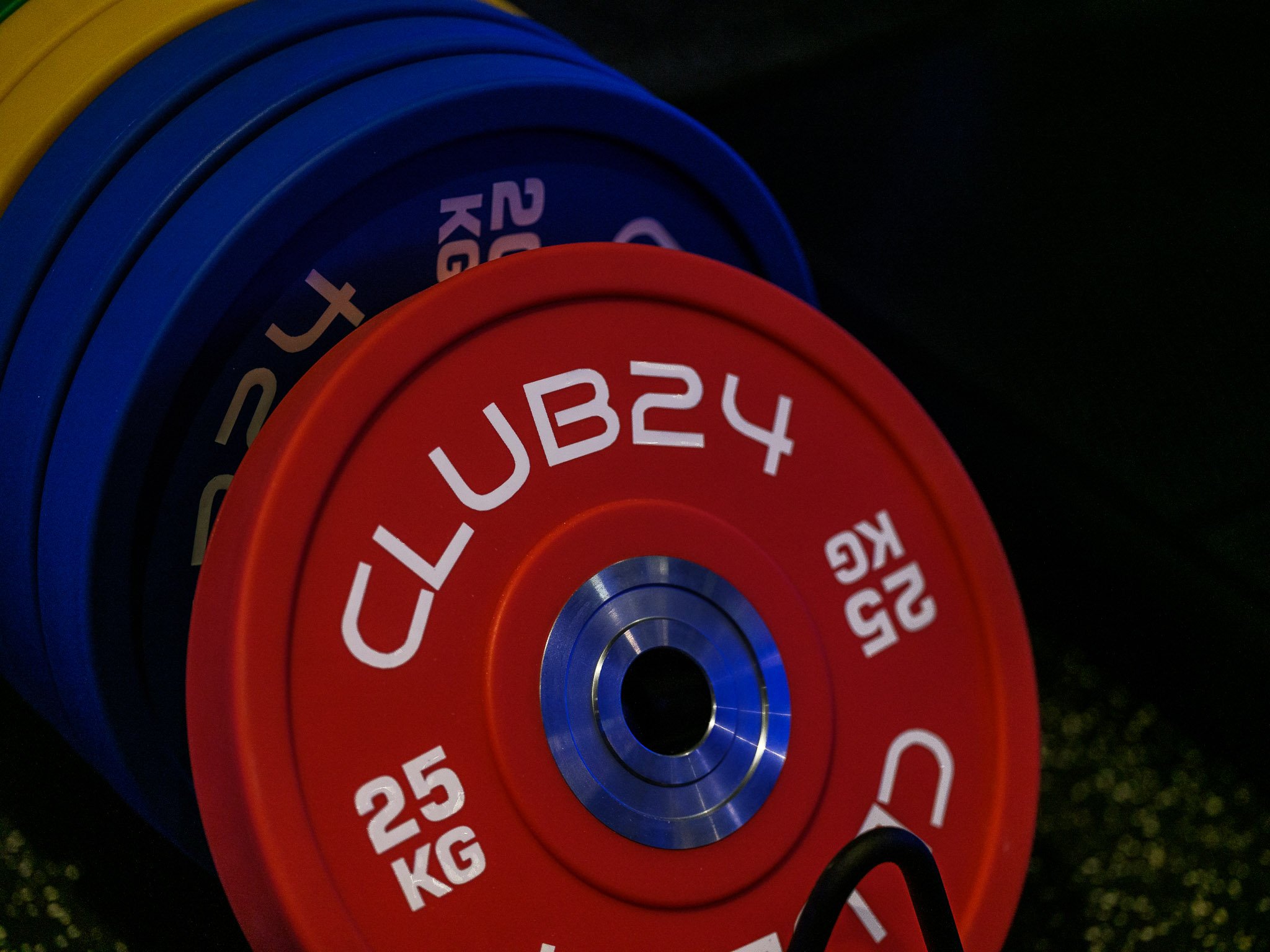 Colorful weight plates stacked, with a red plate labeled '25 KG' and 'CYCUB24' visible, against a dark background.