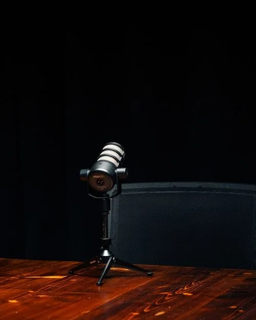 A small black and gray microphone on a tripod stand placed on a wooden table with a dark background.