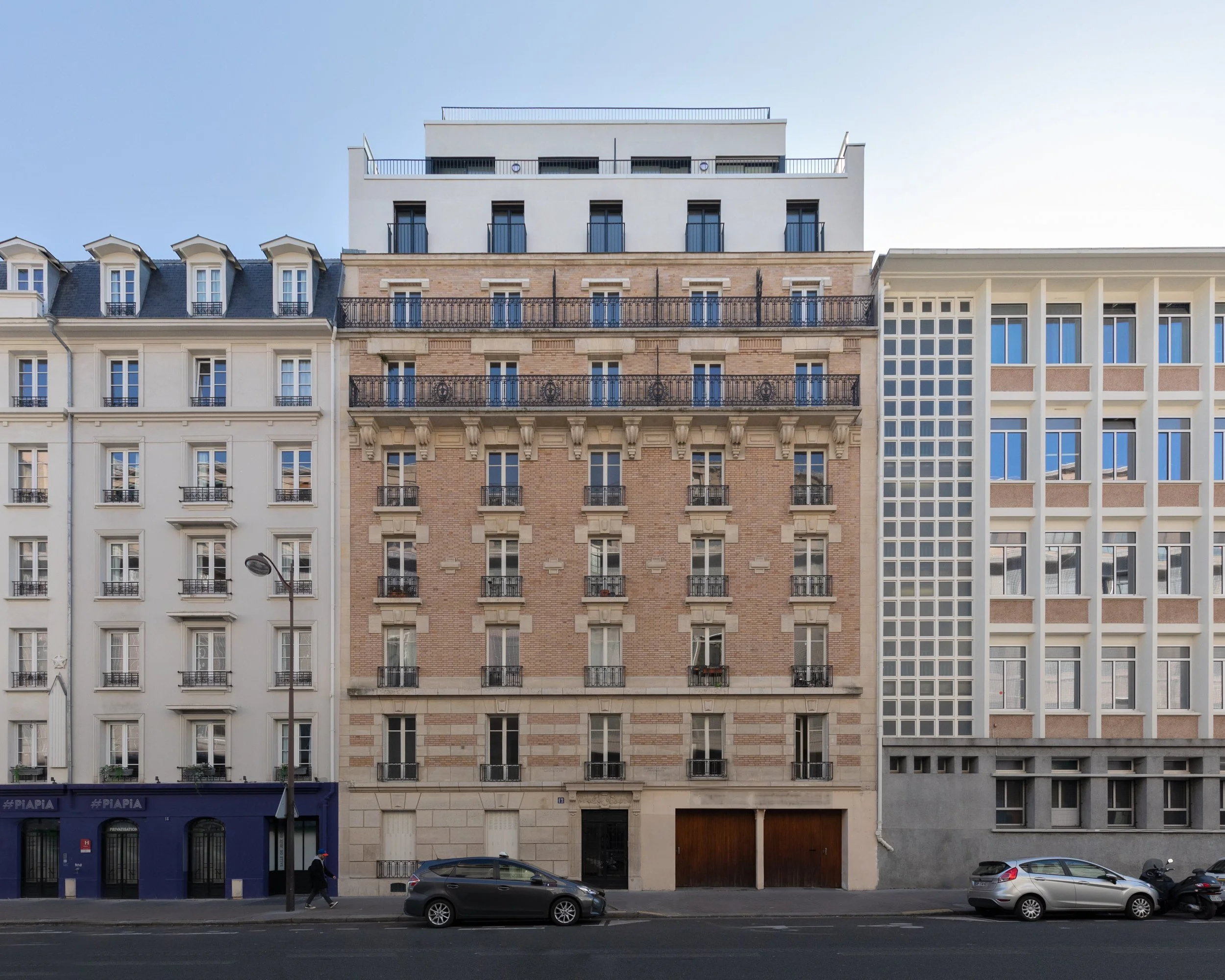 Façade de bâtiments résidentiels modernes avec différentes architectures, voitures stationnées, et un piéton sur le trottoir.