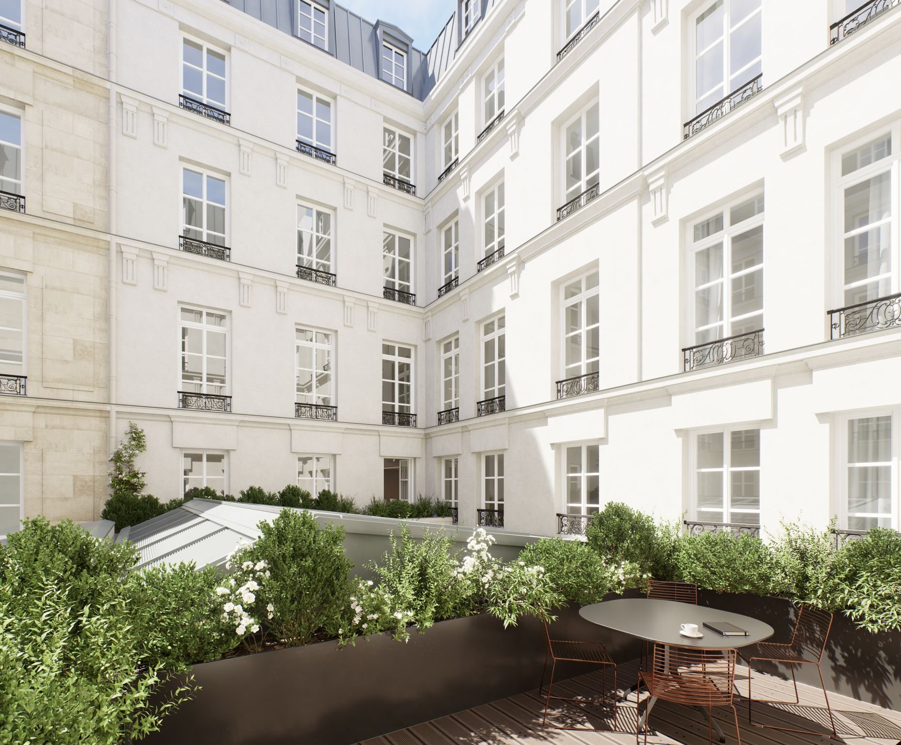 Cour intérieure d'immeuble haussmannien avec jardins et terrasse, où se trouve une table ronde avec quatre chaises en métal et une tasse, entourée de plantes vertes.