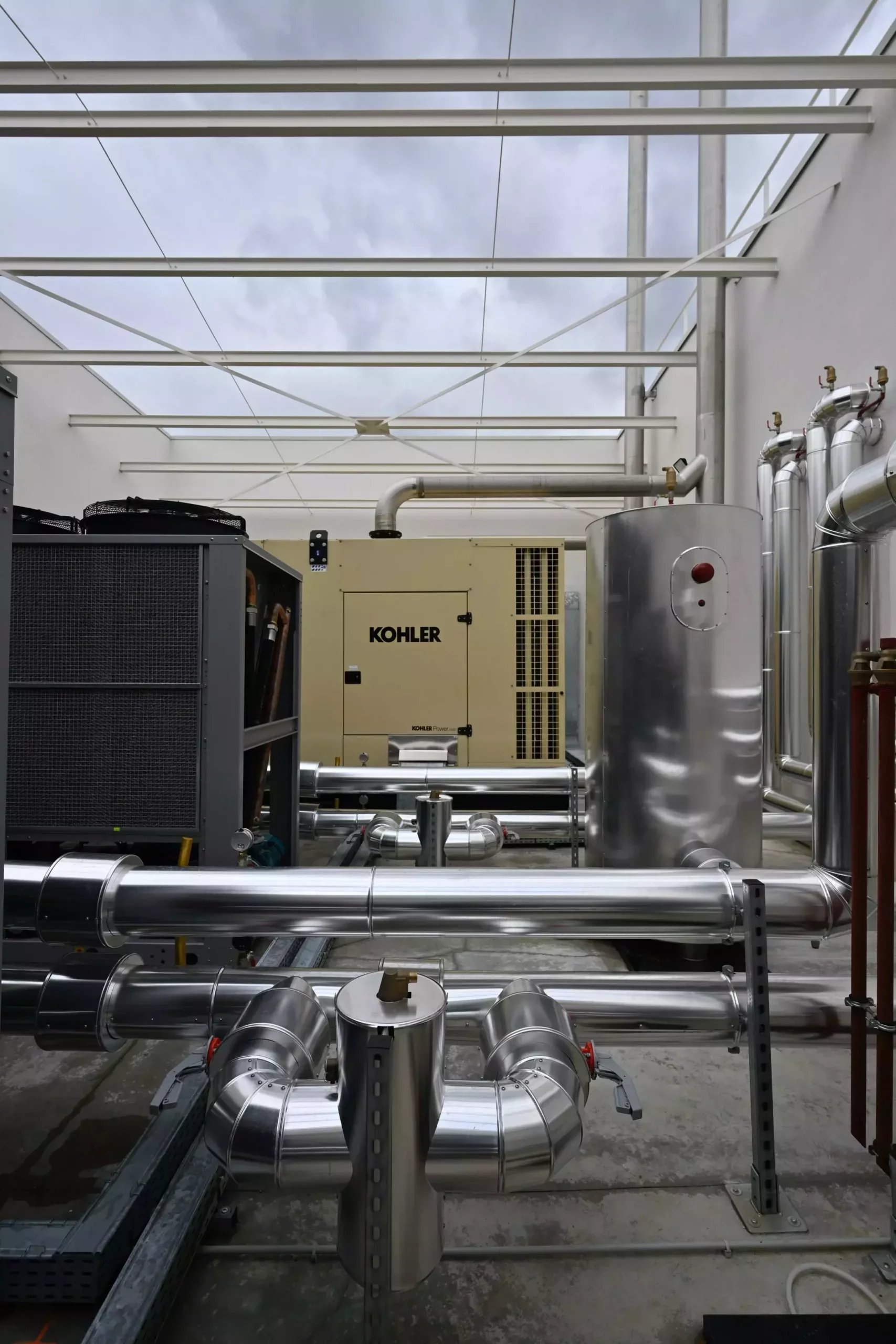 Installation industrielle avec des tuyaux en métal, un réservoir et une machine Kohler sous un toit en verre.