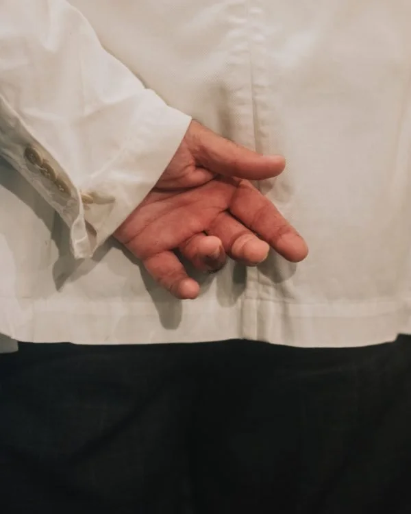 Close-up of a person's hand with fingers crossed, resting against a white coat or shirt.