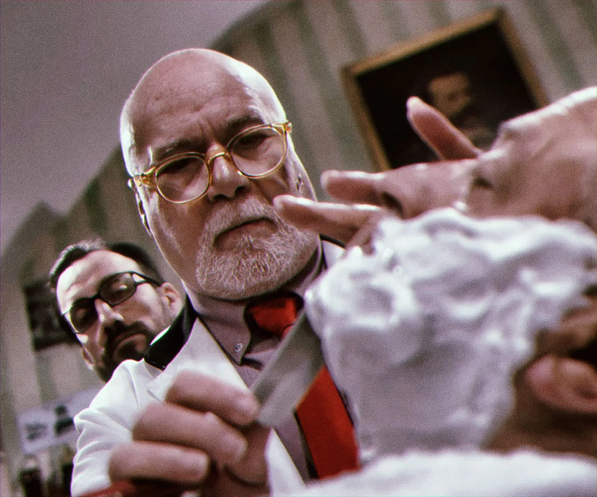 Close-up of an elderly man with glasses, a white beard, and a white coat, reaching into a box of whipped cream. A younger man with glasses is in the background, observing.