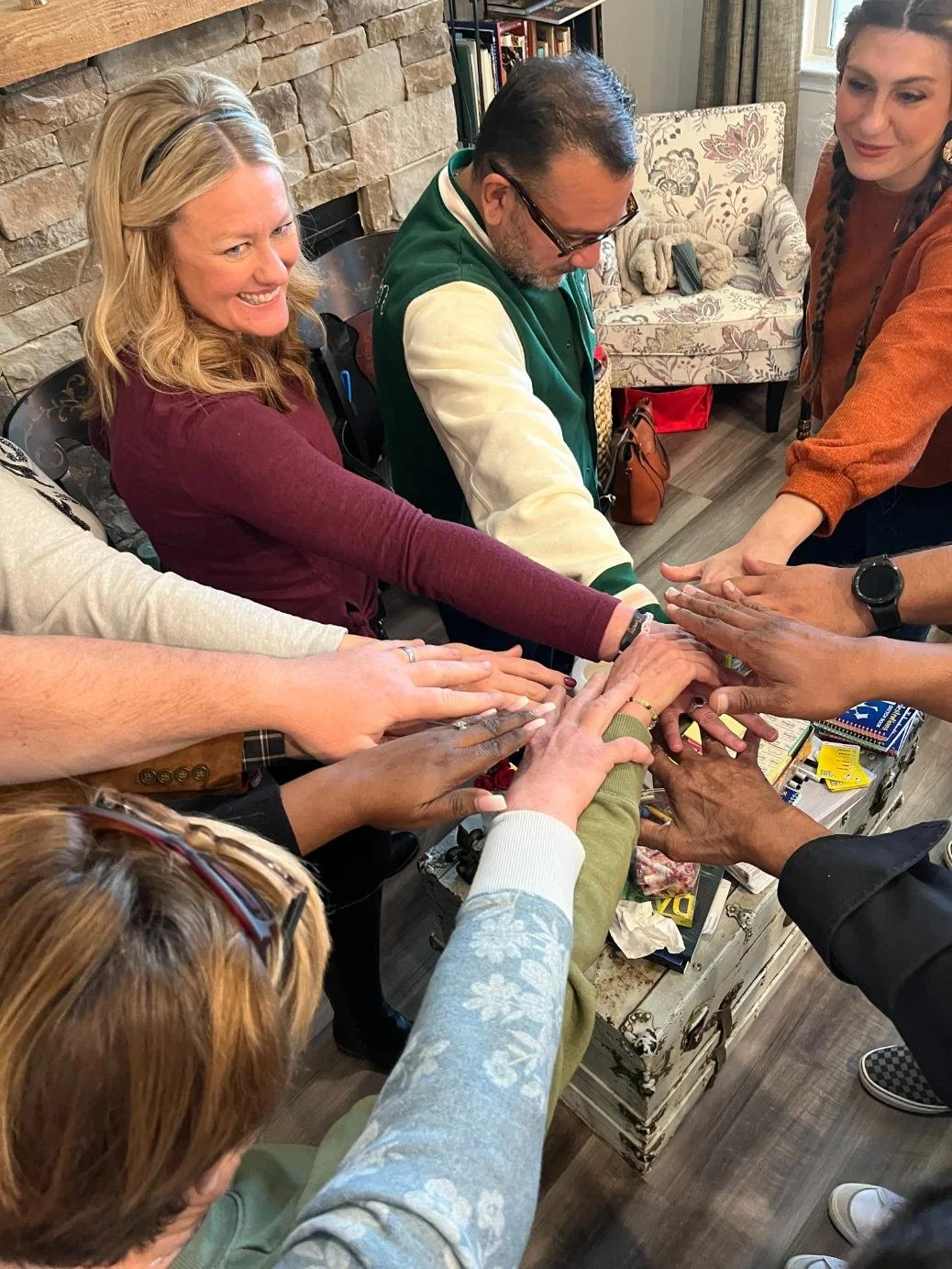 Group of people putting their hands together in a show of teamwork and unity in a cozy indoor setting.
